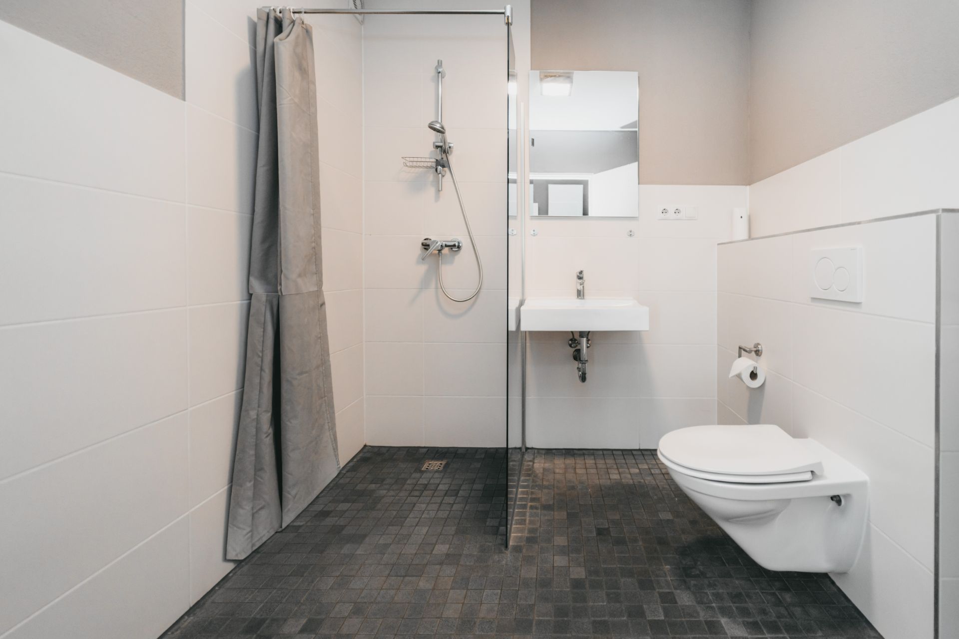 Modernes Badezimmer mit bodengleicher Dusche, Waschbecken, Spiegel und Wandtoilette.