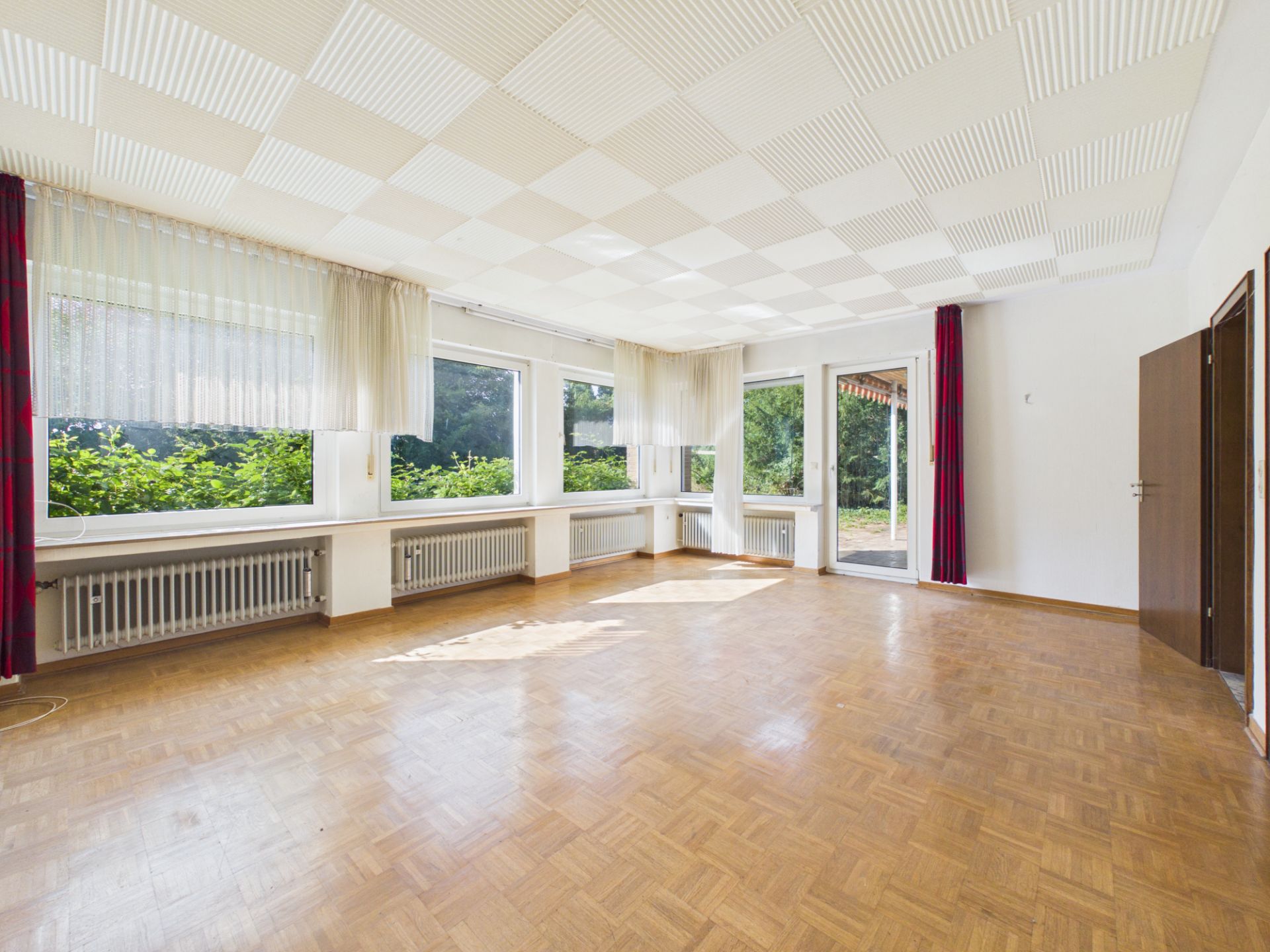 Heller, leerer Raum mit Parkettboden, großen Fenstern und Zugang zur Terrasse.