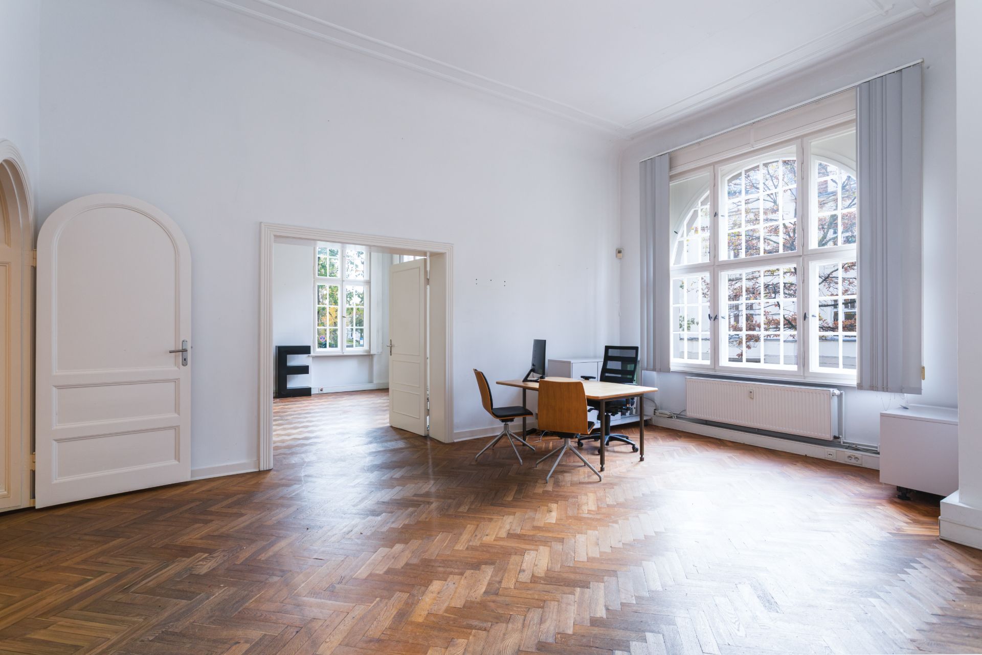 Helles Wohnzimmer mit Parkettboden, großem Fenster und einem Tisch mit zwei Stühlen.