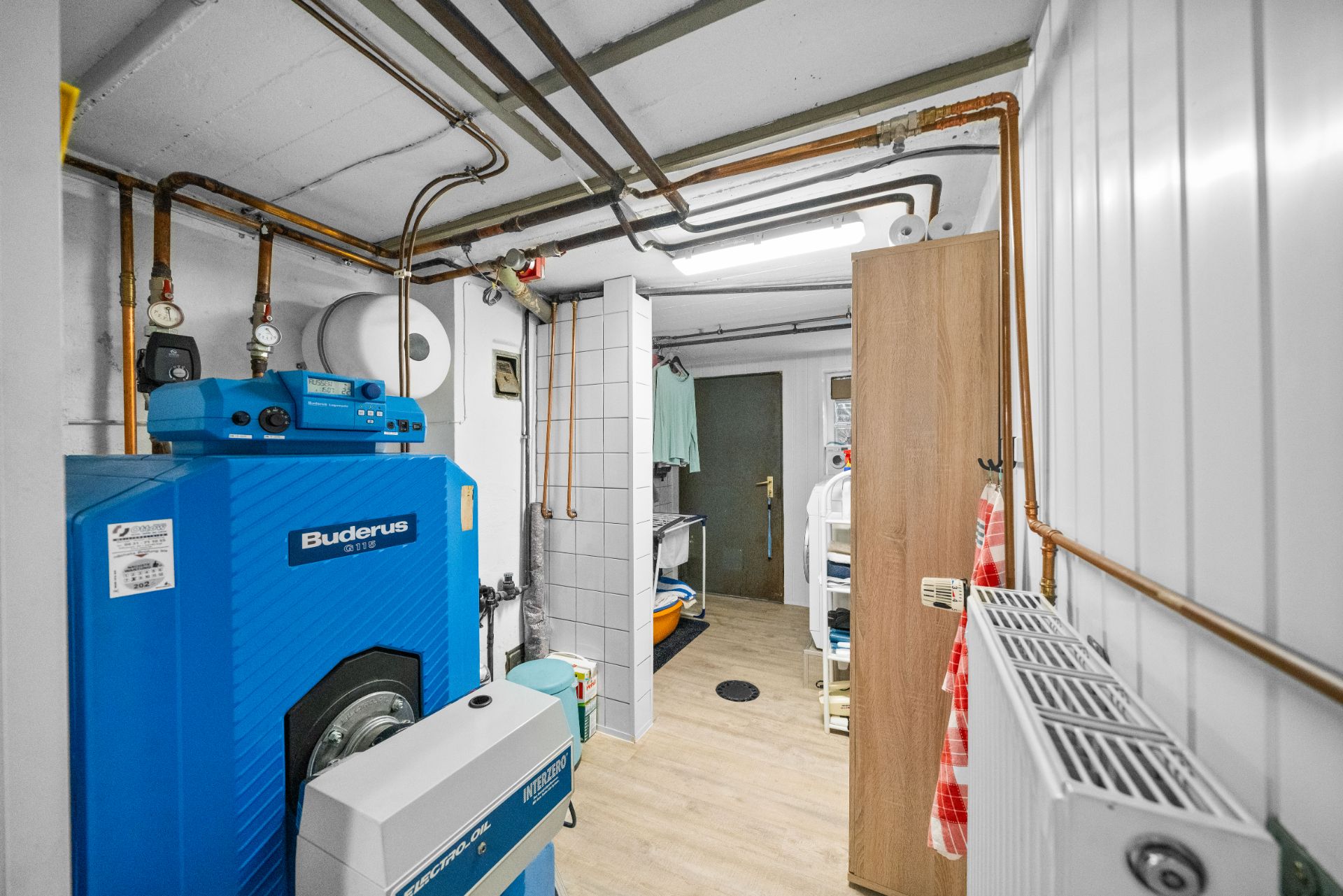 Heizungsraum mit blauer Heizungsanlage, Rohren und Heizkörper an der Wand.