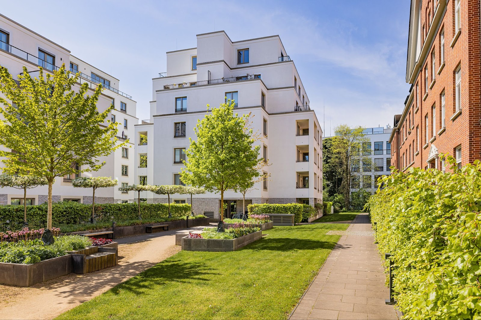 Moderner Innenhof mit Grünflächen, Wegen, Bänken und mehreren Wohngebäuden.