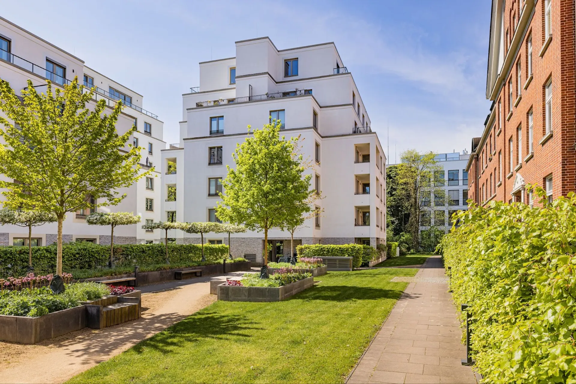 Moderner Innenhof mit Grünflächen, Wegen, Bänken und mehreren Wohngebäuden.