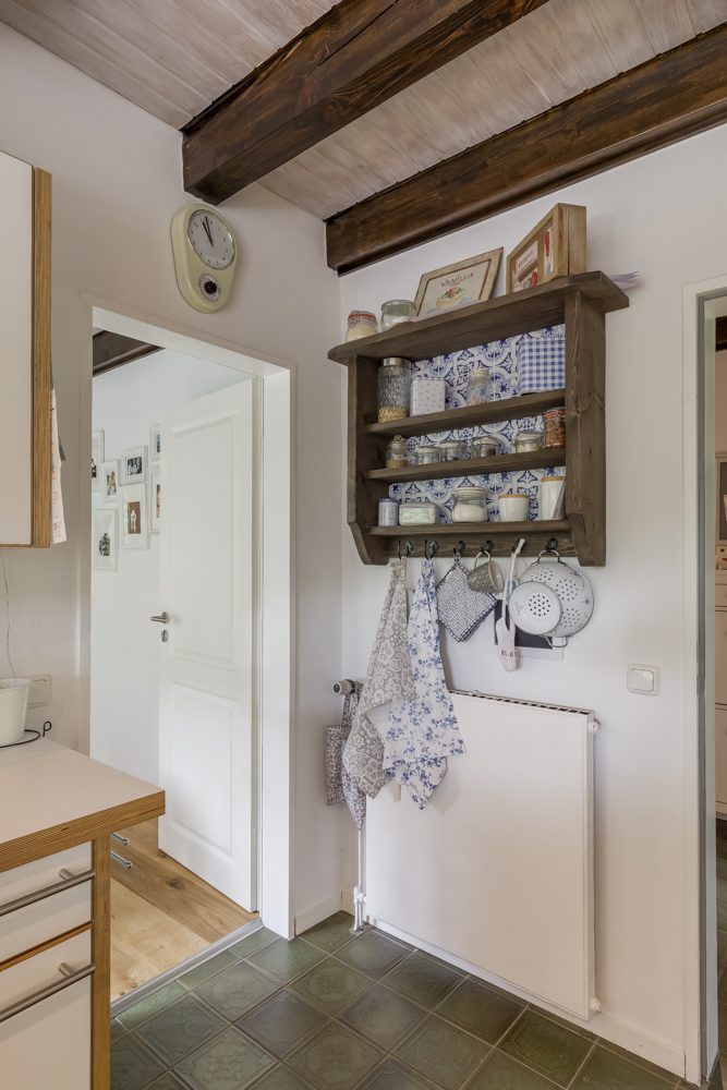 Küchenregal mit Gläsern, Tassen und Handtüchern an Haken an einer weißen Wand unter Holzdecke.
