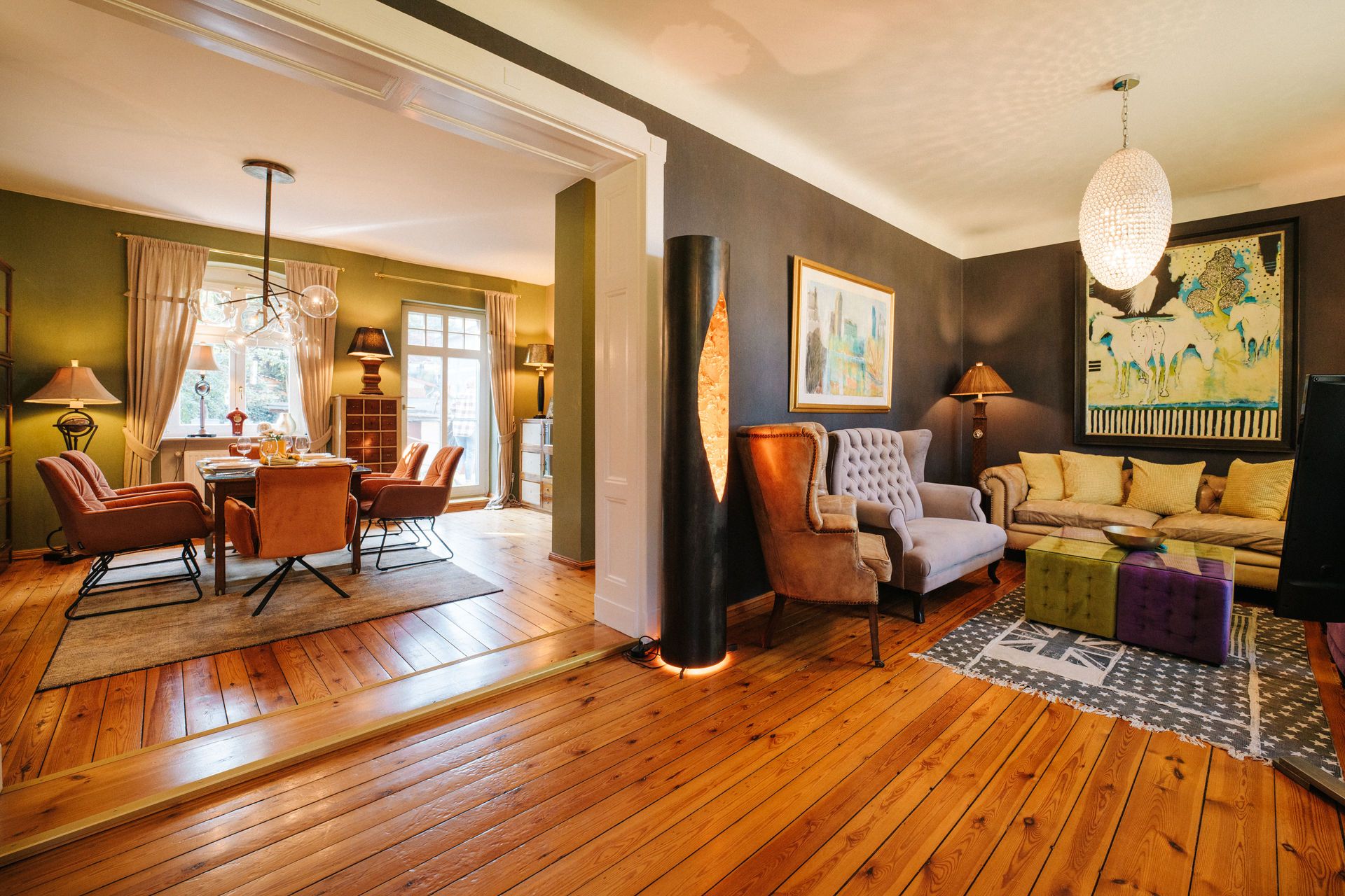 Wohnzimmer mit Holzboden, modernen Sesseln und Sofa, offener Durchgang zum Essbereich mit großen Fenstern.