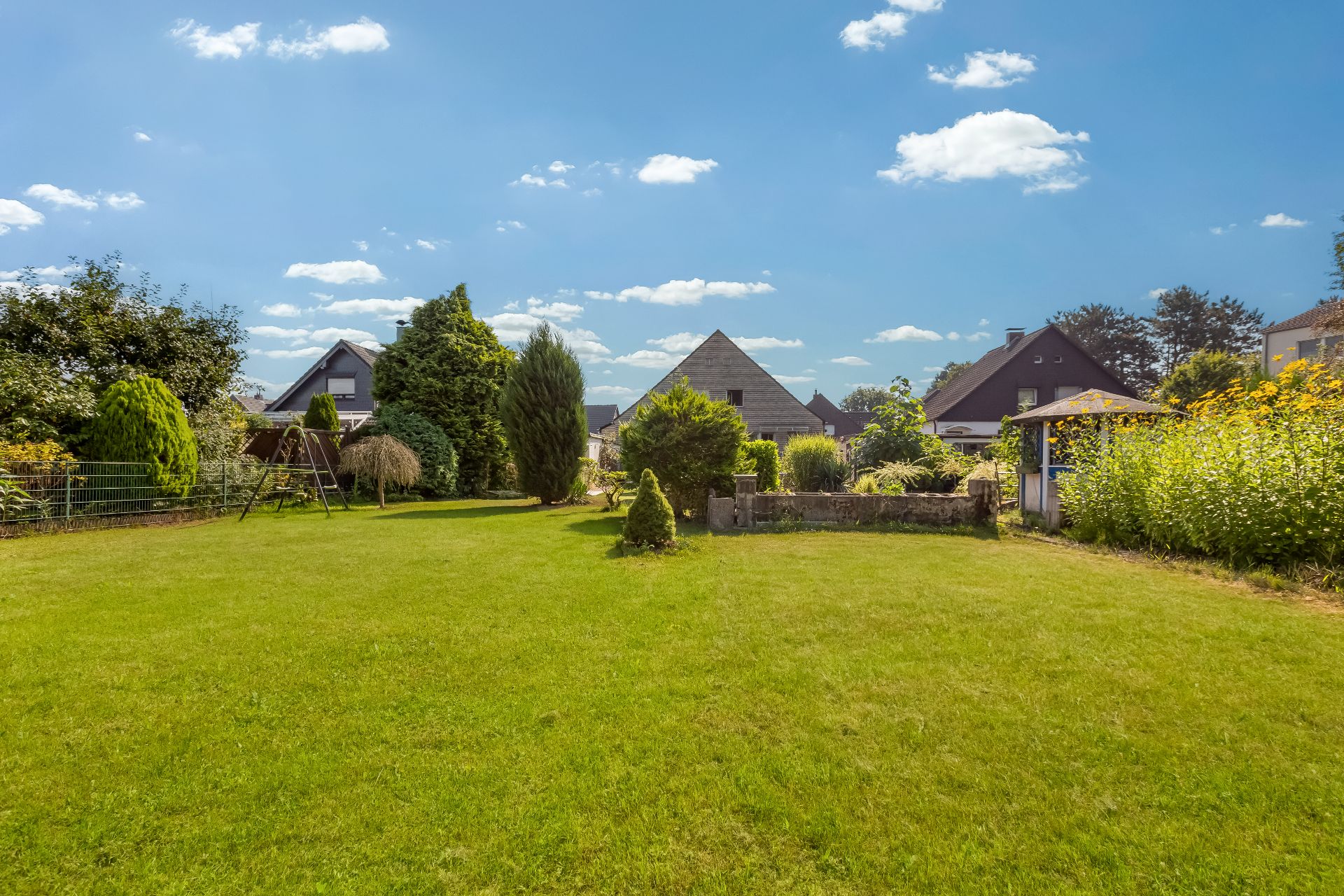 Großer gepflegter Garten mit Rasenfläche, Sträuchern, Schaukel und Gartenhaus bei Einfamilienhäusern.