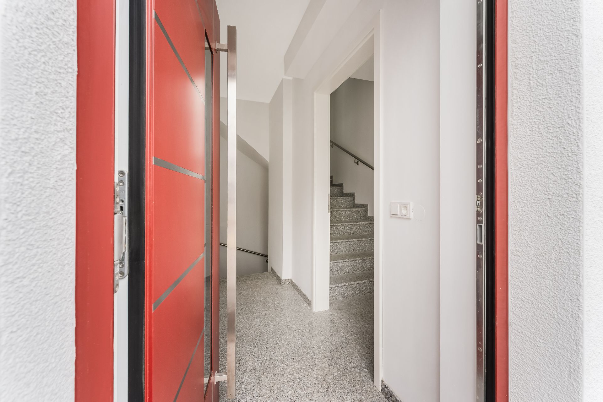 Offene rote Haustür, Blick auf hellen Flur mit Treppe nach oben.