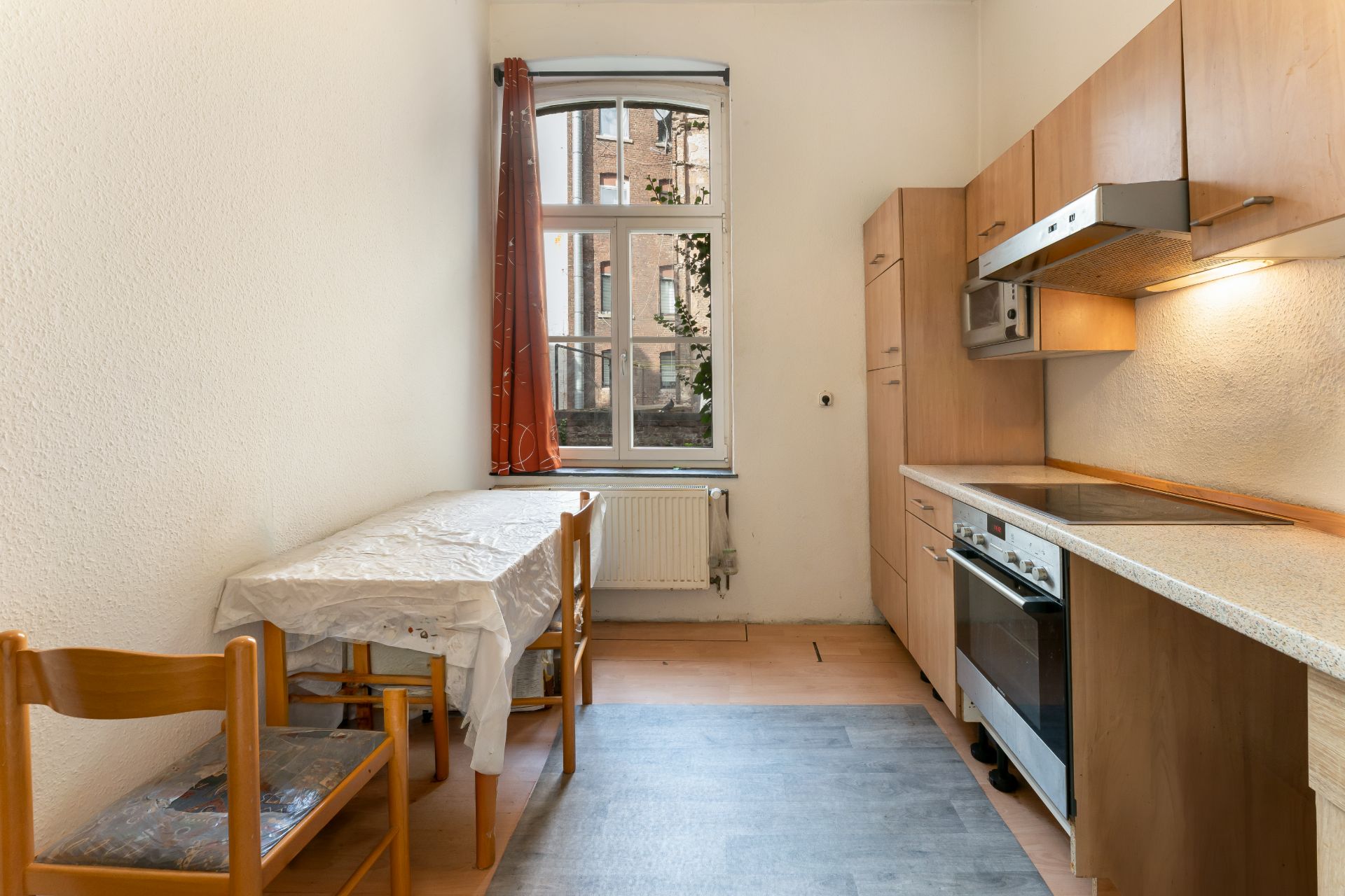 Schmale Küche mit Esstisch, zwei Stühlen, Fenster und Einbauküche aus Holz.