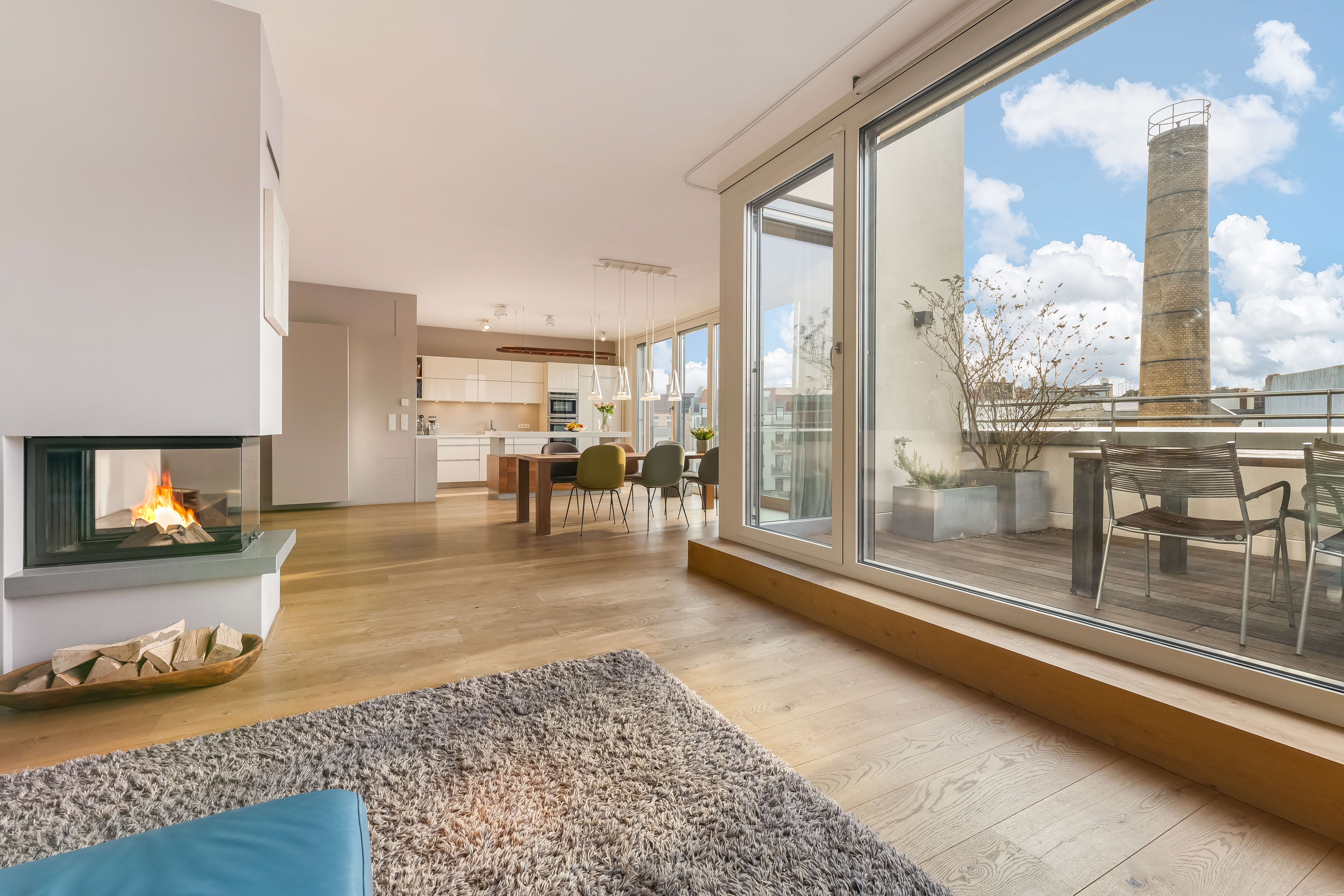 Modernes Wohnzimmer mit Kamin, Essbereich, großer Fensterfront und Zugang zur Terrasse.