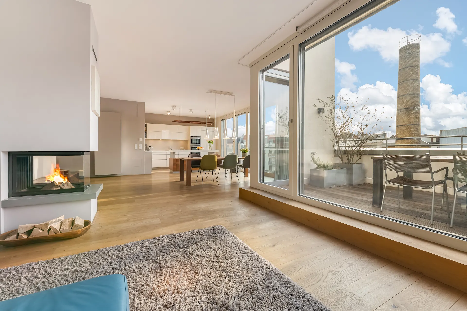 Modernes Wohnzimmer mit Kamin, Essbereich, großer Fensterfront und Zugang zur Terrasse.