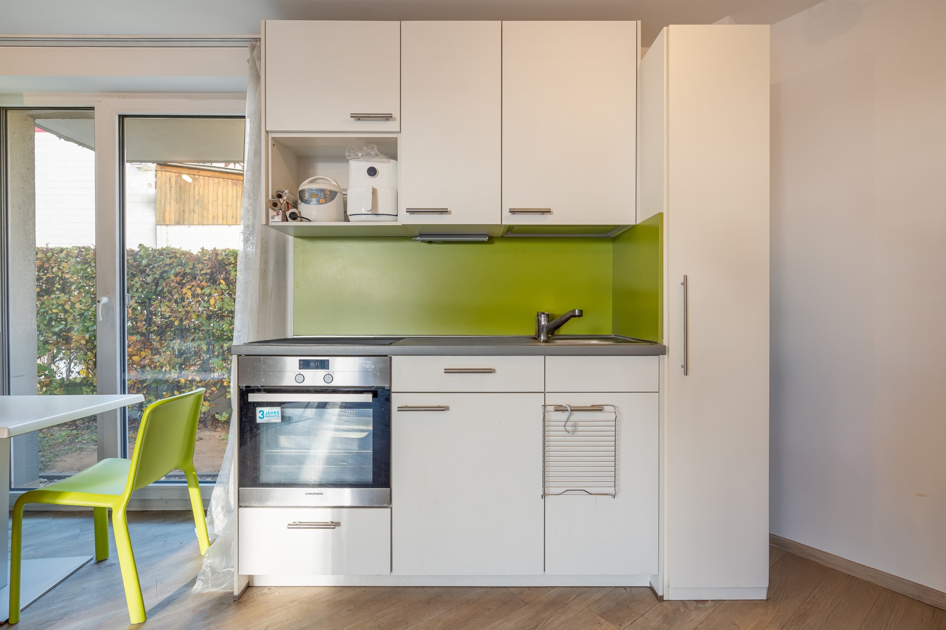Moderne kleine Küche mit weißen Schränken, grünem Spritzschutz, Ofen und Spüle.