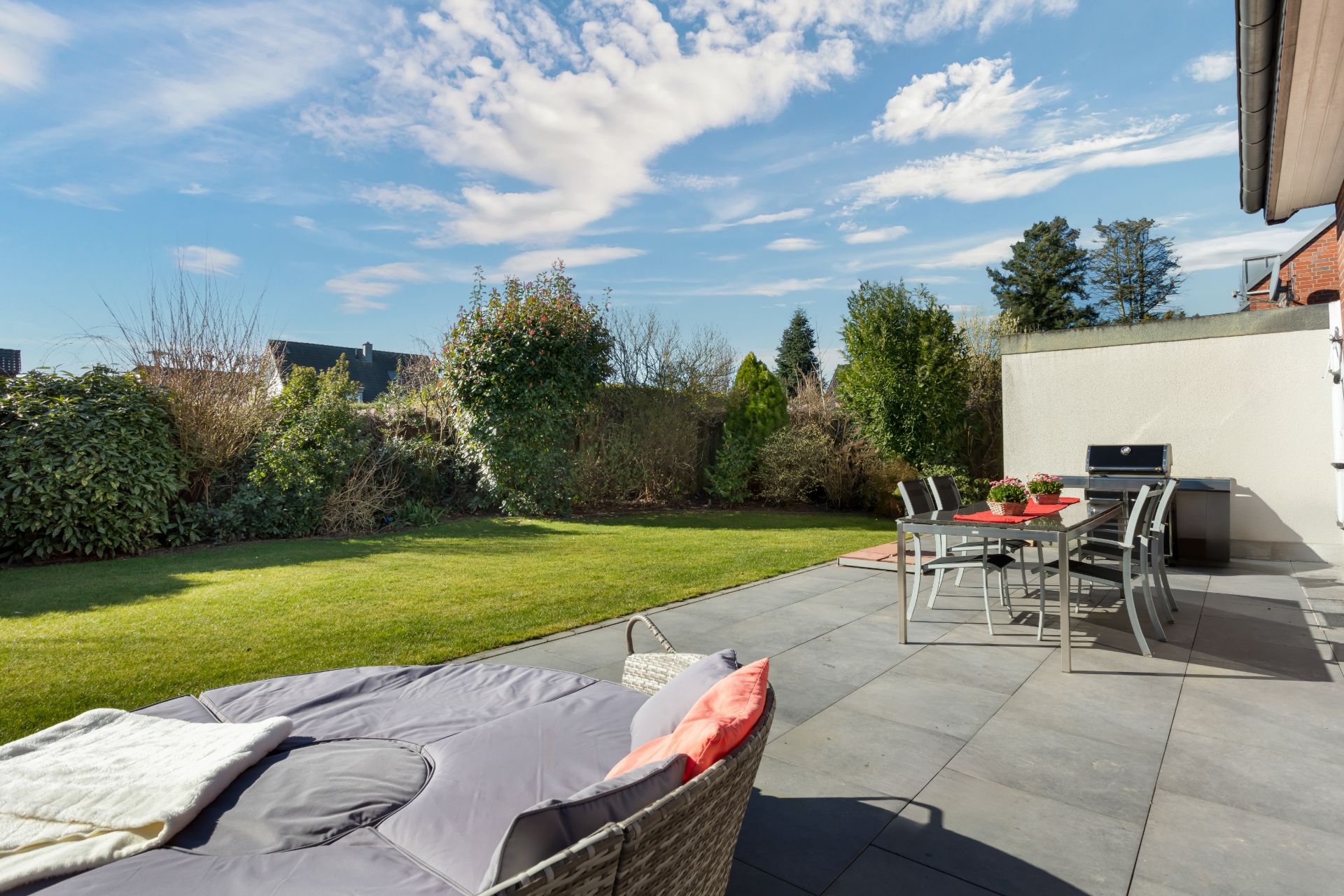Moderne Terrasse mit Esstisch und Stühlen, Liege und Blick auf grünen Garten.