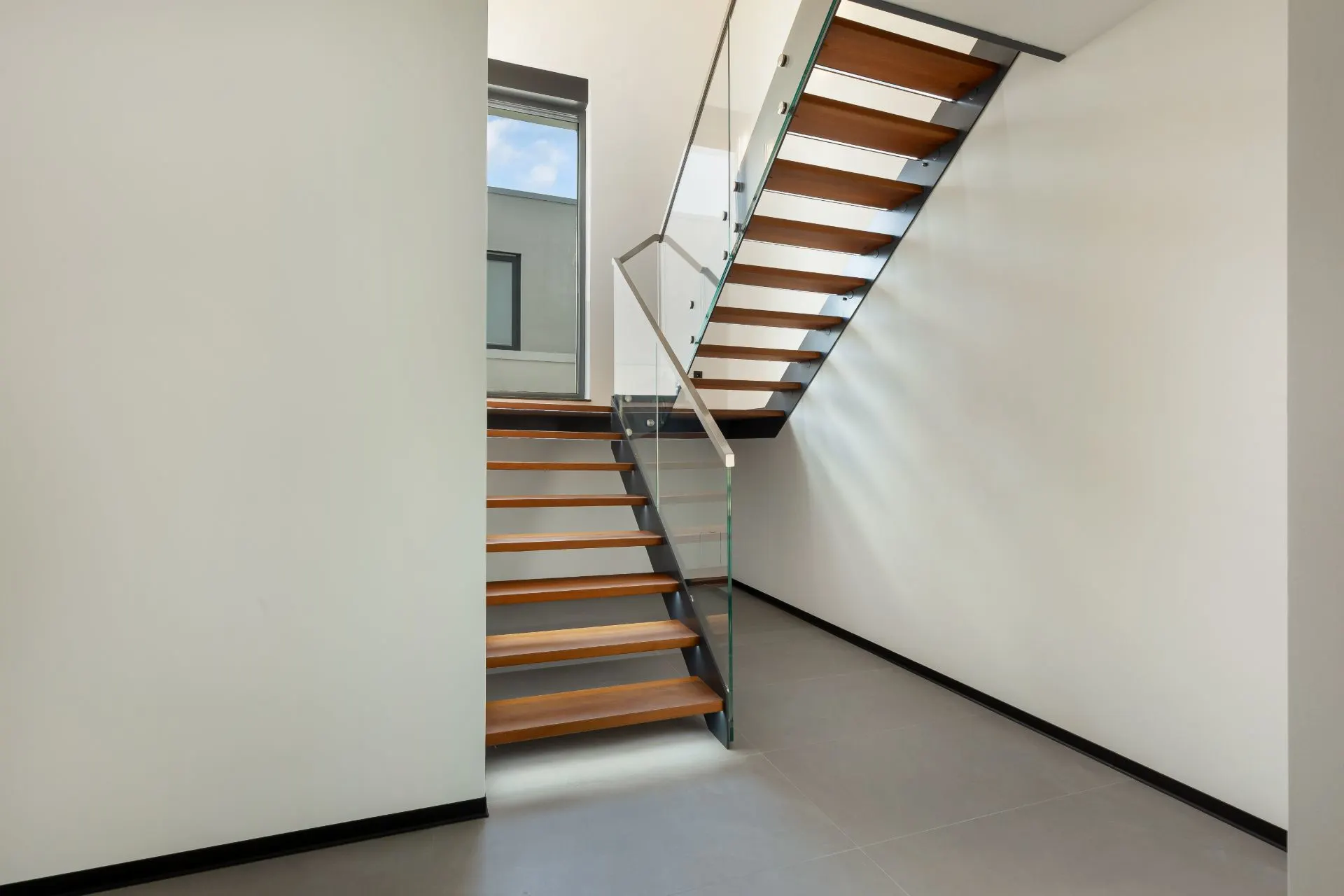 Moderne Holztreppe mit Glasgeländer in einem hellen Flur eines Wohnhauses.
