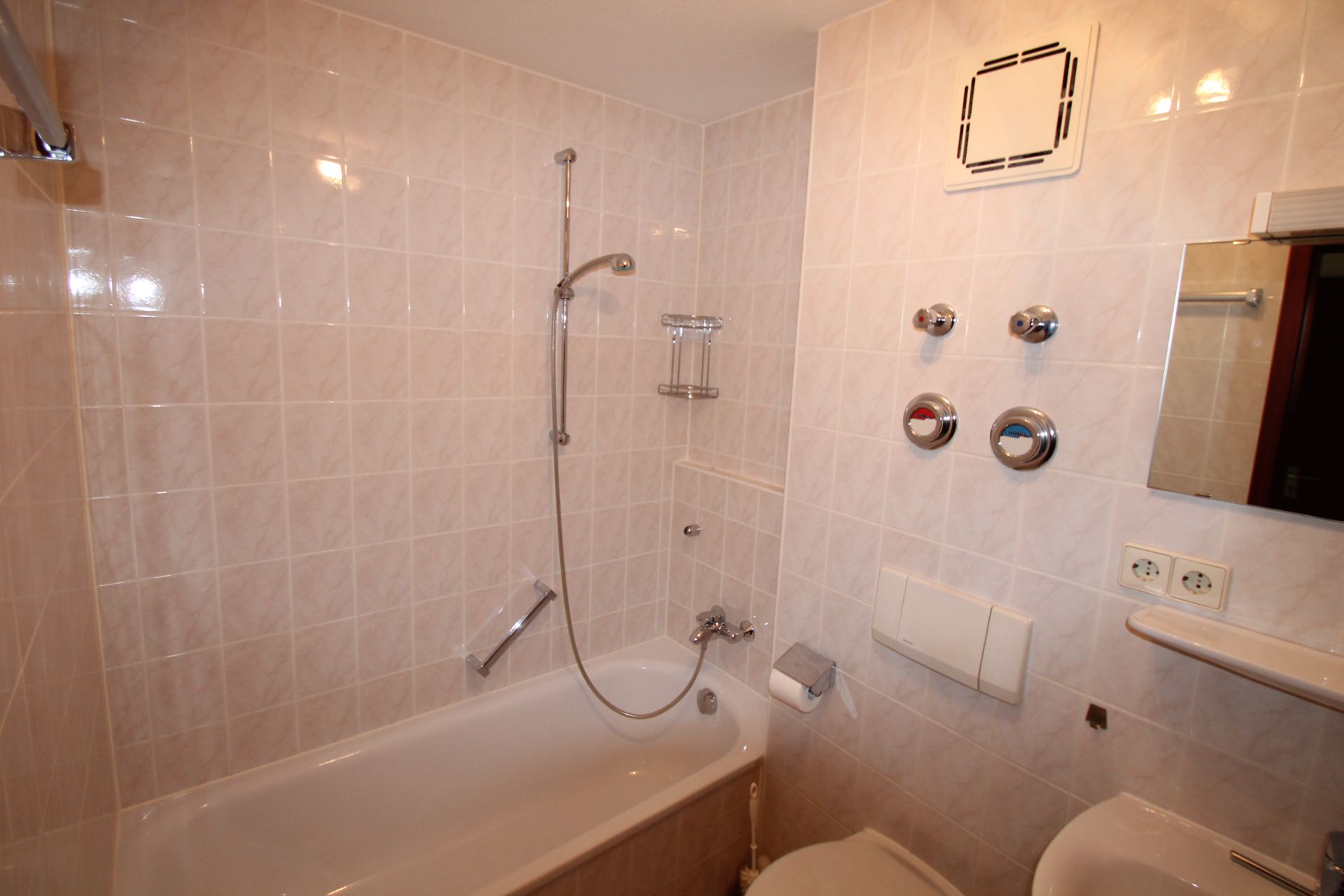 Badezimmer mit Badewanne, Duschkopf, WC und gefliesten Wänden.