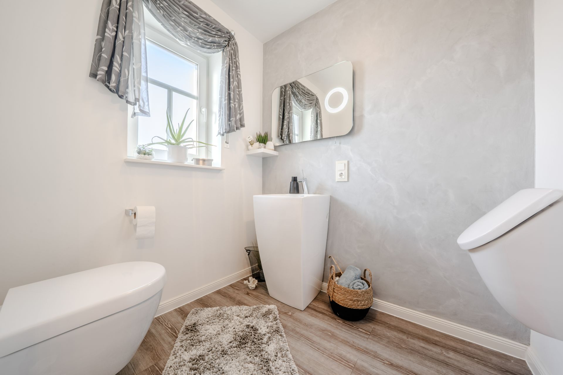 Modernes Badezimmer mit Toilette, Waschbecken, Spiegel, Fenster und grauem Teppich.