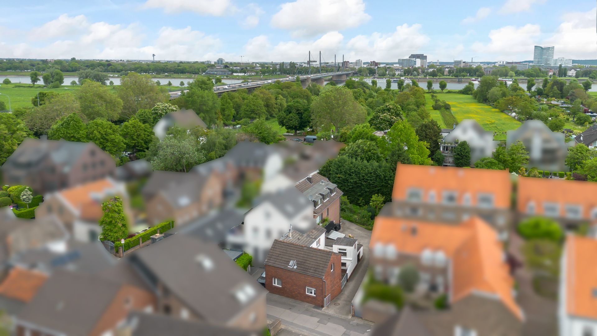 Luftaufnahme eines Wohngebiets mit Häusern, Bäumen und einer Brücke im Hintergrund.