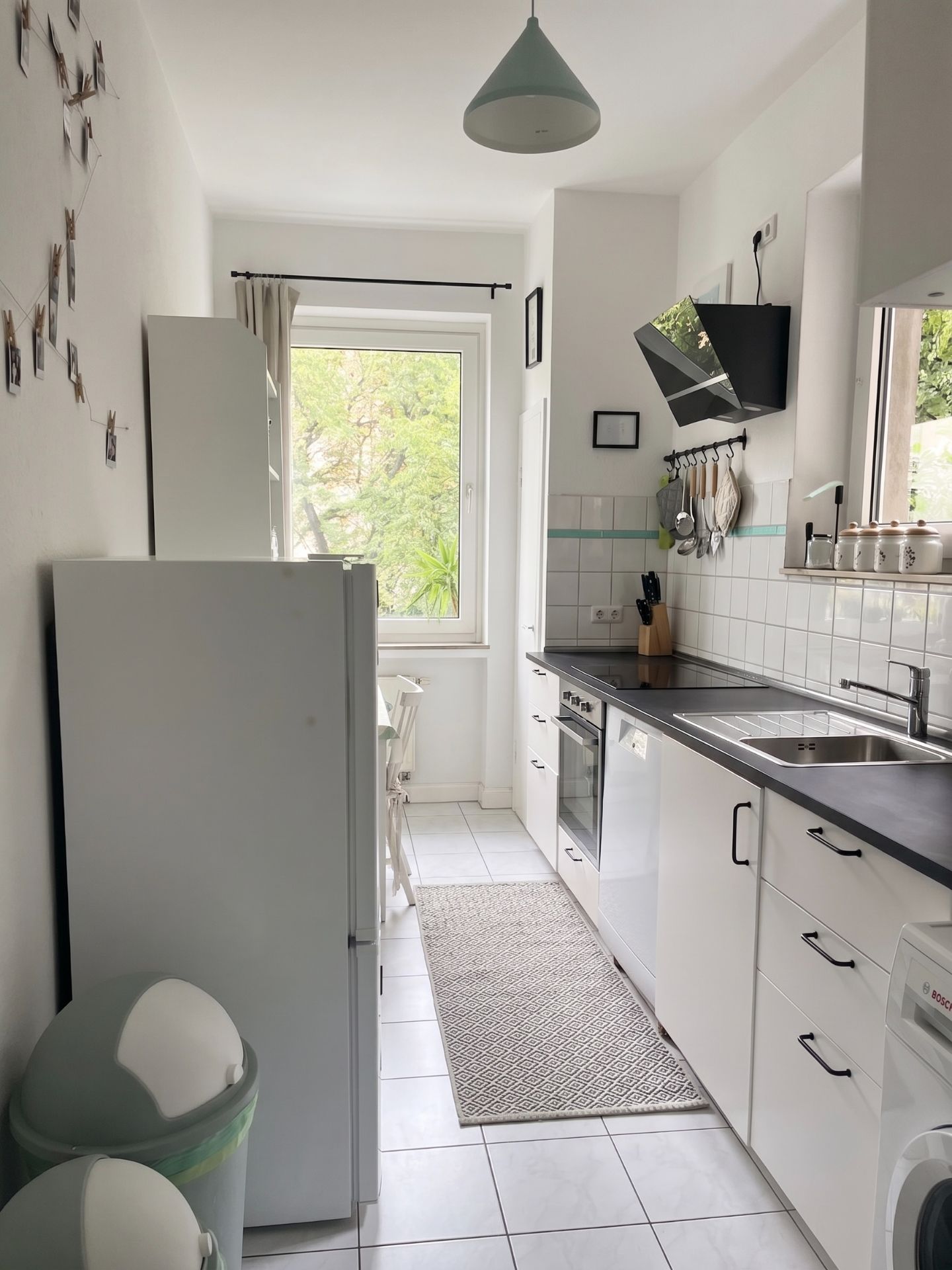 Helle, schmale Küche mit weißen Schränken, Geräten, Fenster und Wanddekoration.