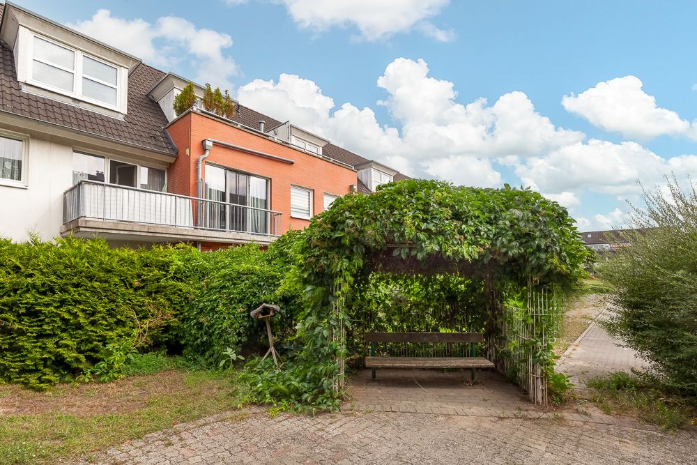 Wohnhaus mit Balkon, davor eine überdachte Gartenbank mit Rankpflanzen.