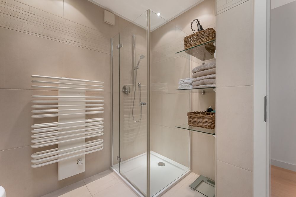 Modernes Badezimmer mit Glasdusche, Handtuchheizkörper und Regalen mit Handtüchern und Körben.