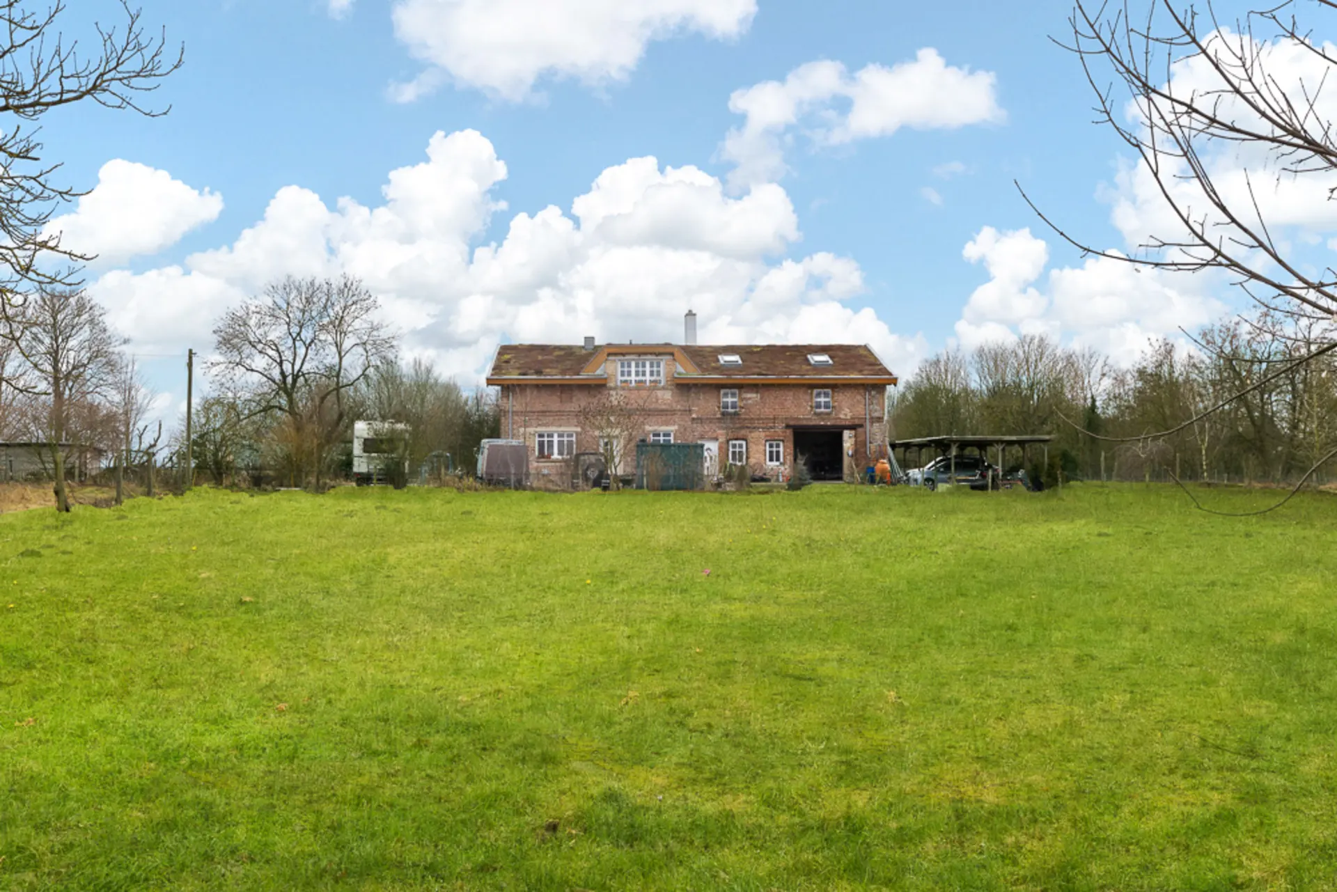 Backsteinwohnhaus mit großem Garten, umgeben von Bäumen unter blauem Himmel.