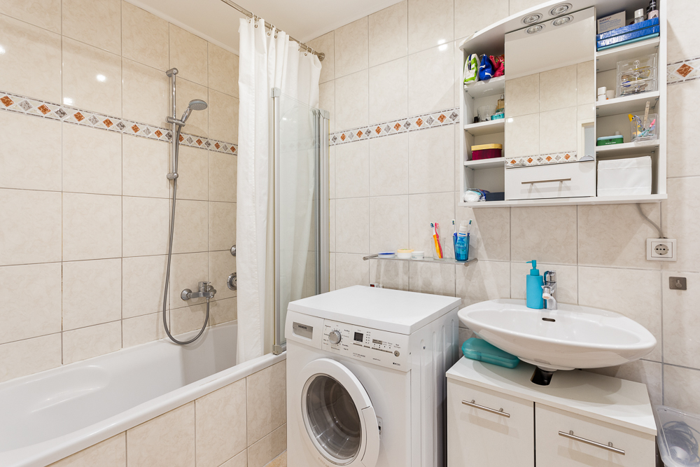 Helles Badezimmer mit Badewanne, Waschmaschine, Waschbecken und Spiegelschrank.