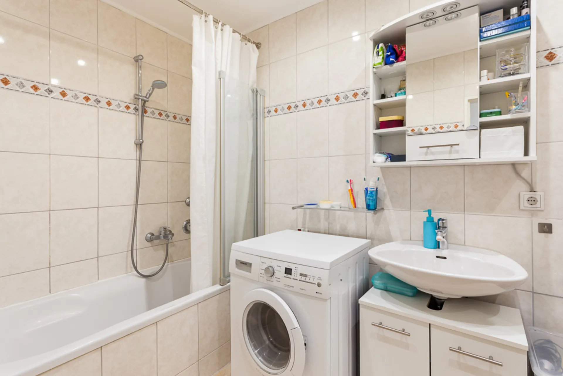 Helles Badezimmer mit Badewanne, Waschmaschine, Waschbecken und Spiegelschrank.