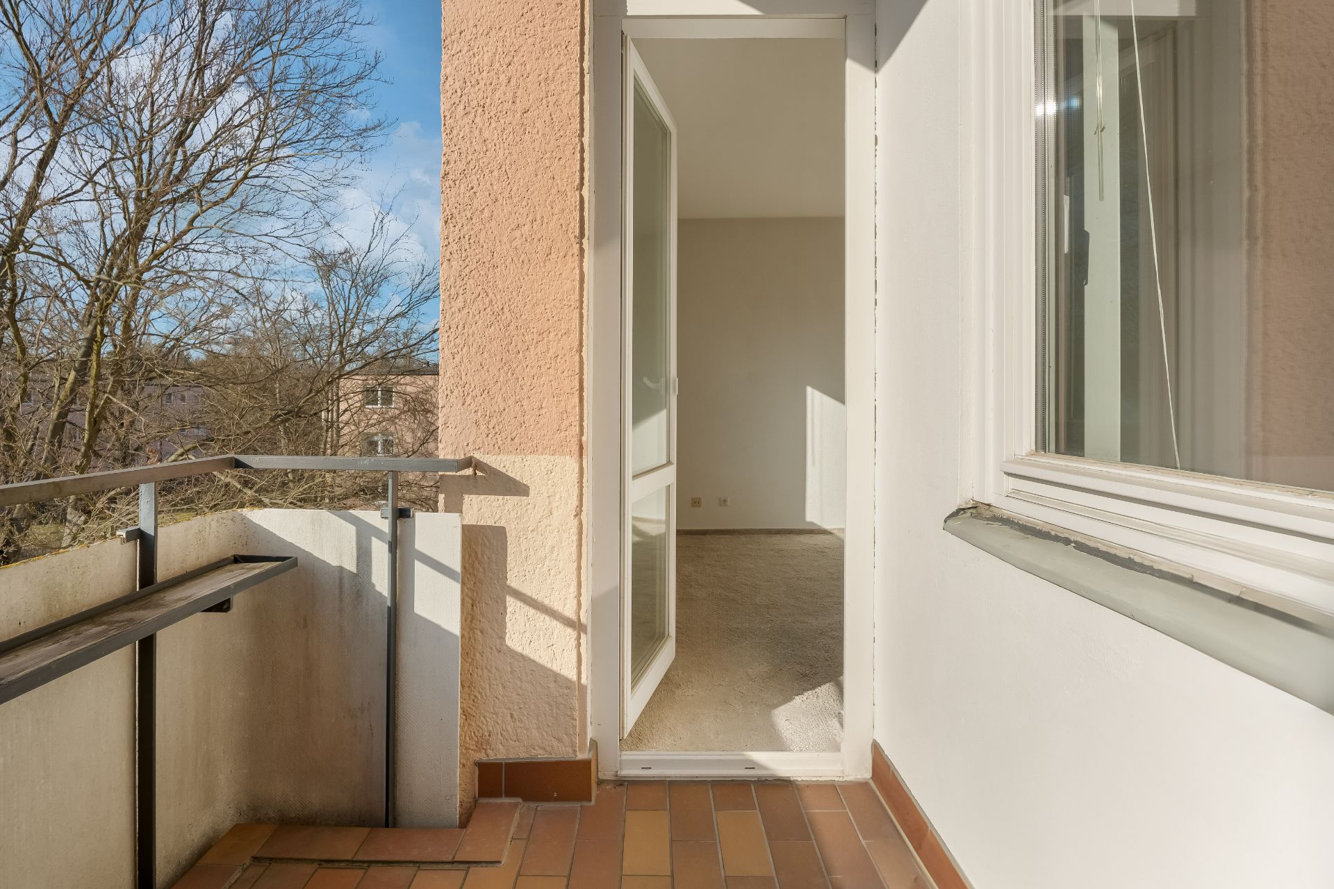 Kleiner Balkon mit gemauertem Geländer und Blick durch offene Tür in ein leeres Zimmer.