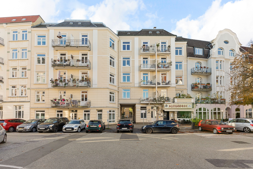 Mehrstöckiges Wohnhaus mit Balkonen und parkenden Autos davor.