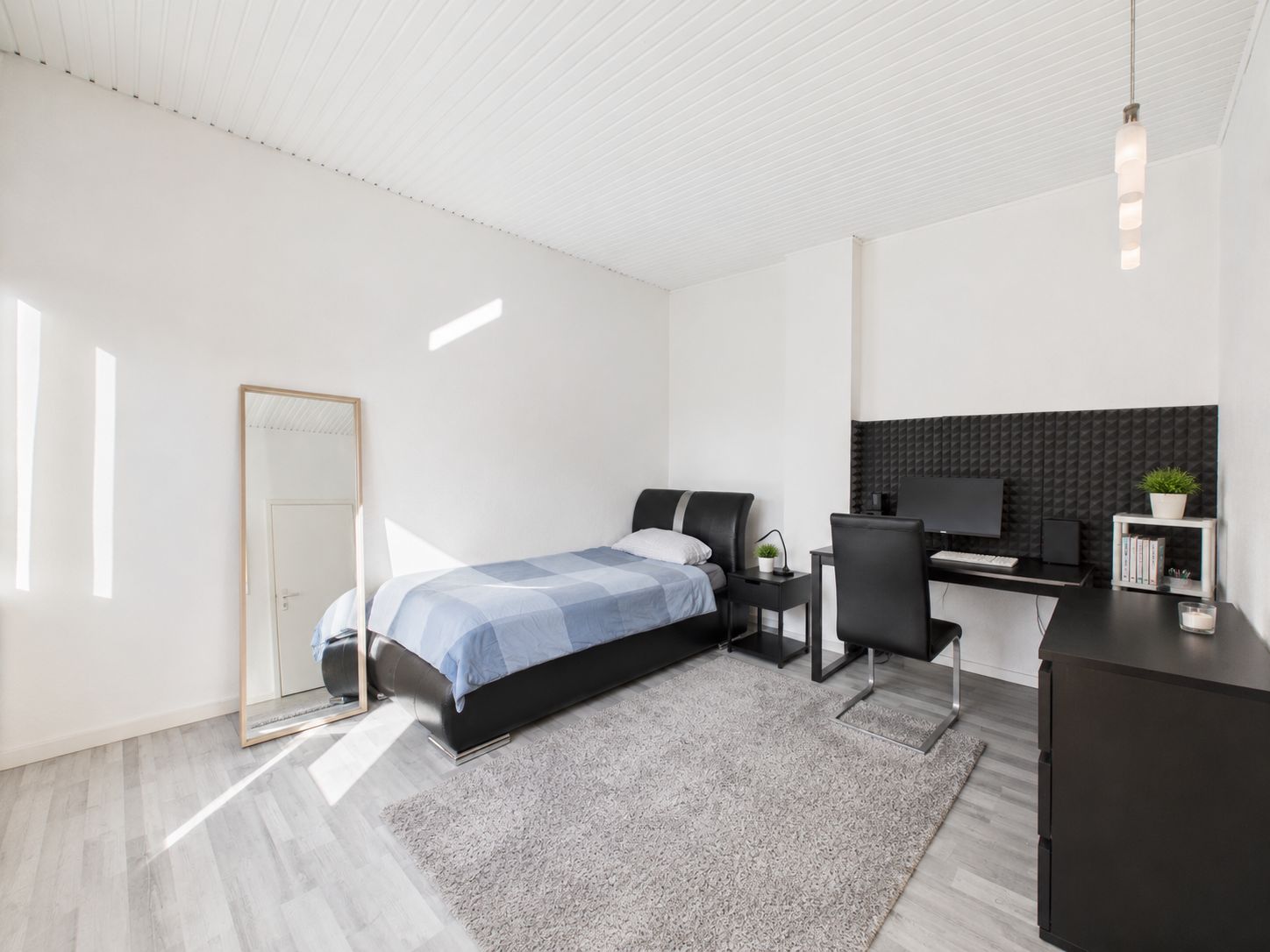 Helles Schlafzimmer mit Einzelbett, Schreibtisch, Stuhl, Spiegel und Teppich.