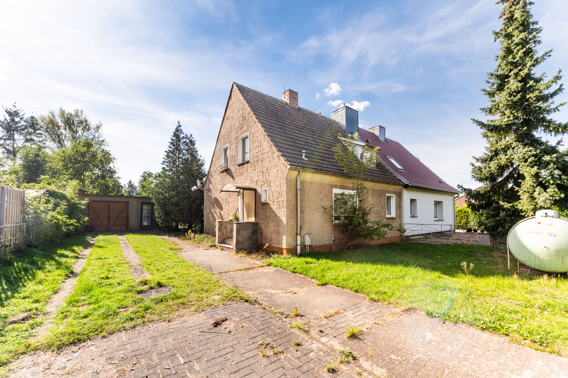 Zweistöckiges Wohnhaus mit Garten, Weg zum Haus und Bäumen im Hintergrund.