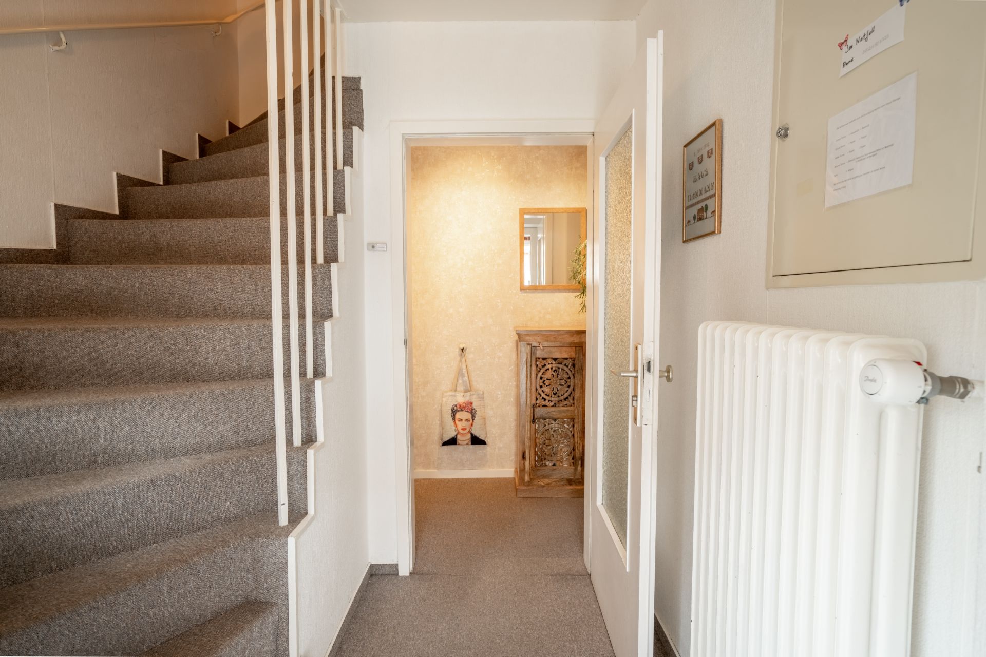 Ein Flur mit Treppe, Heizung und einem kleinen Schrank mit Spiegel im Hintergrund.