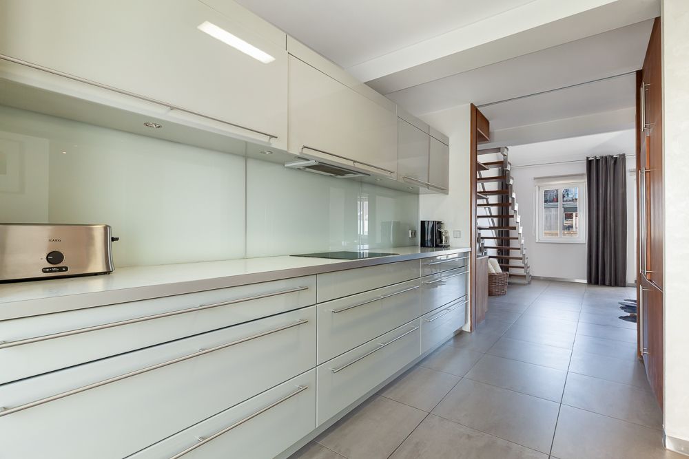 Moderne, helle Küche mit weißen Schränken, Toaster, Treppe und Fenster im Hintergrund.