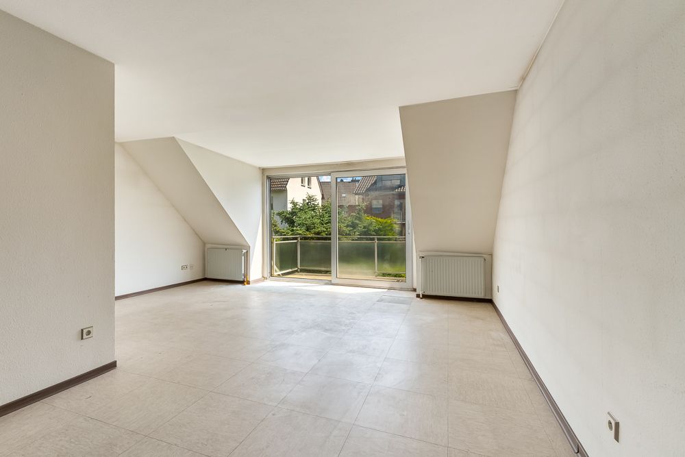 Helles, leeres Zimmer mit Fliesenboden, Heizkörpern und großen Fenstern mit Blick nach draußen.