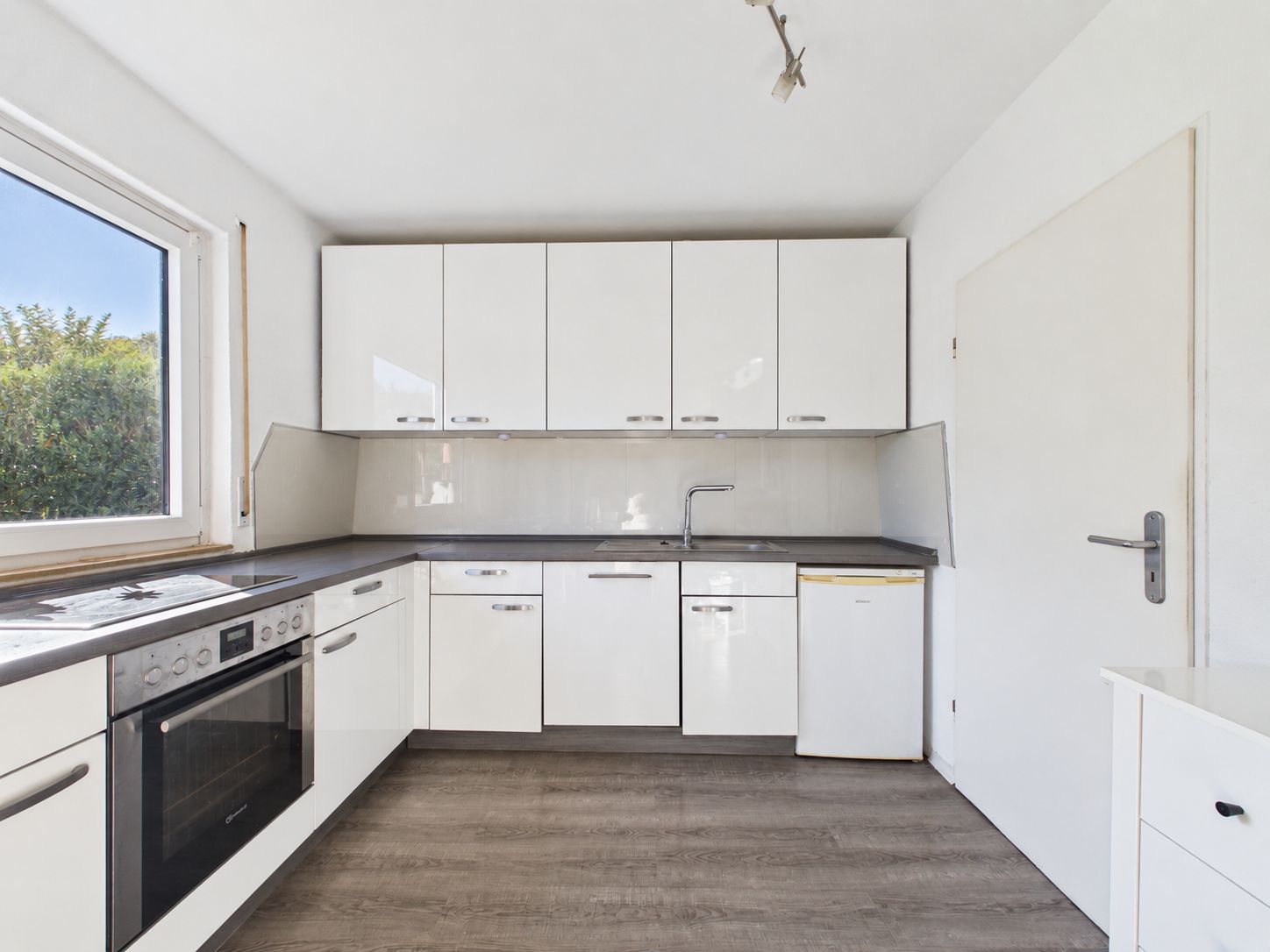 Moderne weiße Einbauküche mit großem Fenster, Herd, Spüle und Kühlschrank.