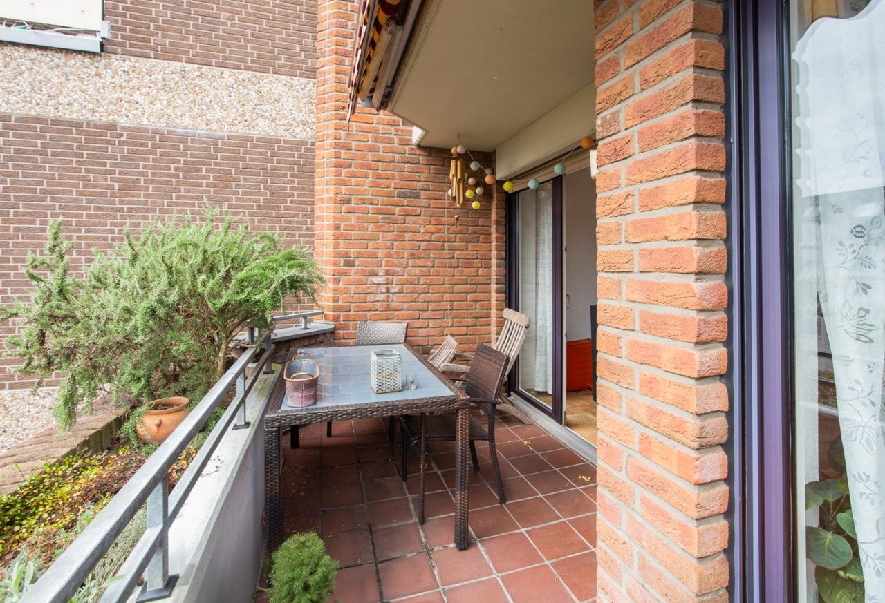 Überdachter Balkon mit Glastisch, Stühlen und Pflanze, umgeben von Backsteinmauern.