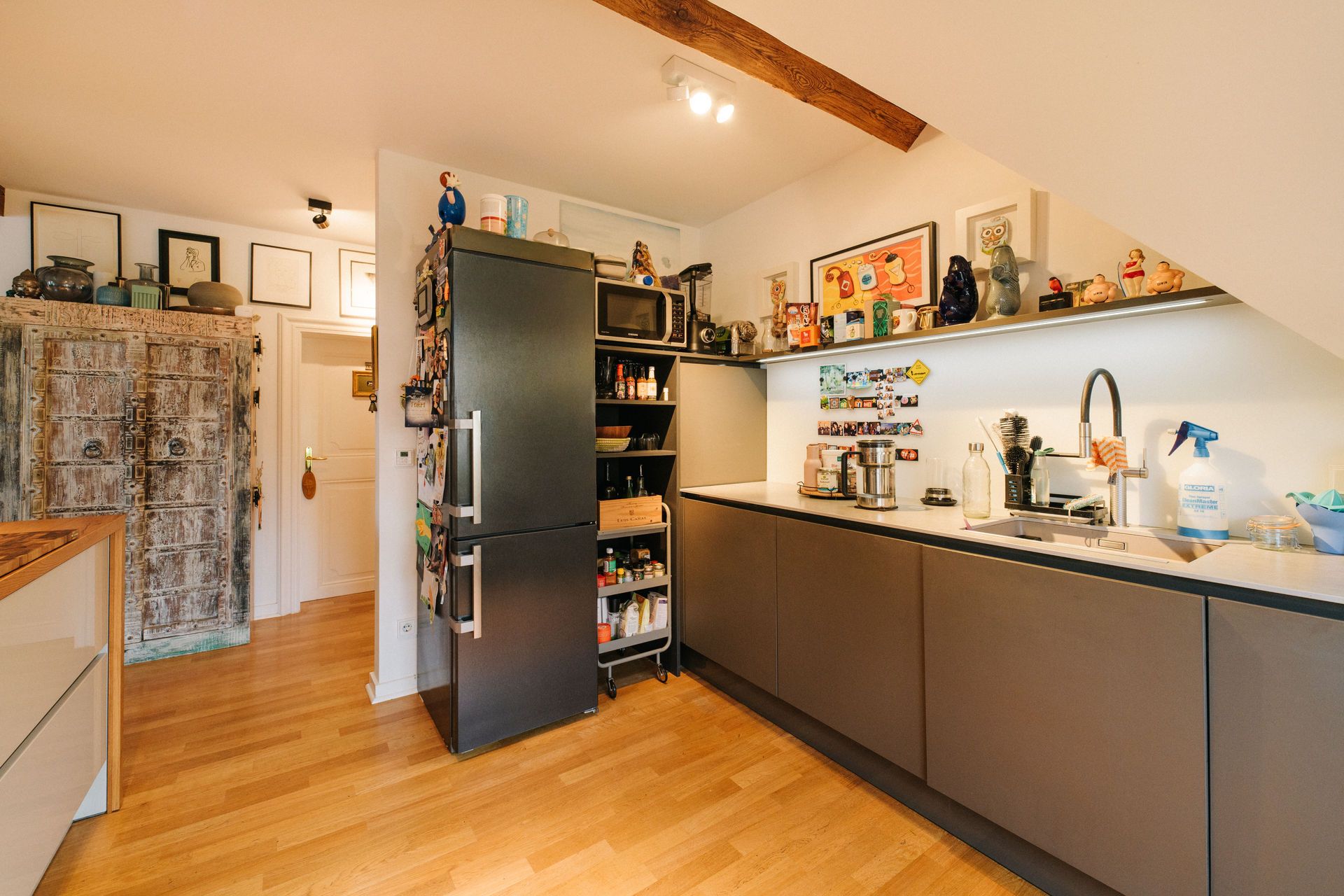 Moderne Küche mit Holzboden, dunklen Schränken, Kühlschrank und Dekorationen auf dem Regal.