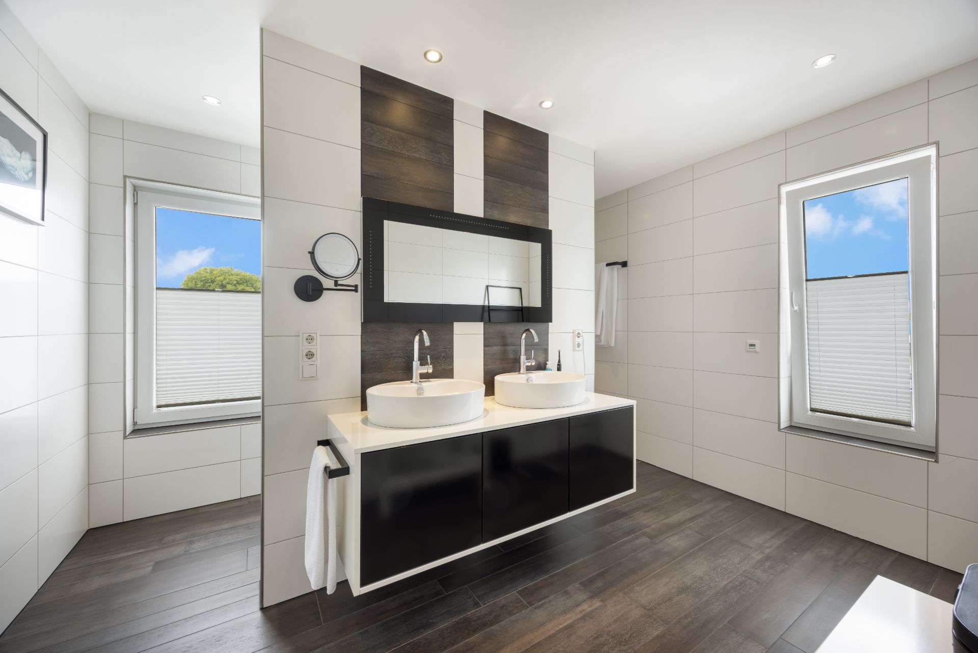 Modernes Badezimmer mit zwei Waschbecken, großem Spiegel und zwei Fenstern mit Außenblick.