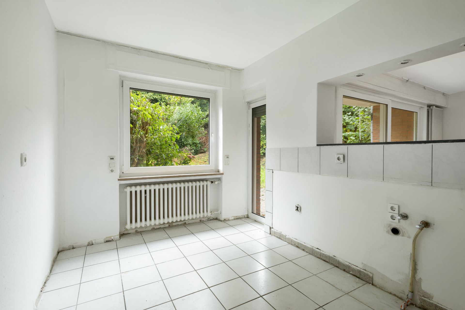 Leerer, weiß gefliester Raum mit großem Fenster und Blick ins Grüne.
