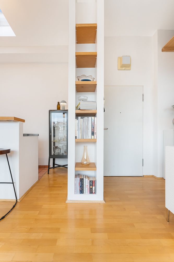 Offenes Regal mit Büchern und Deko in modernem, hellen Raum mit Holzboden.