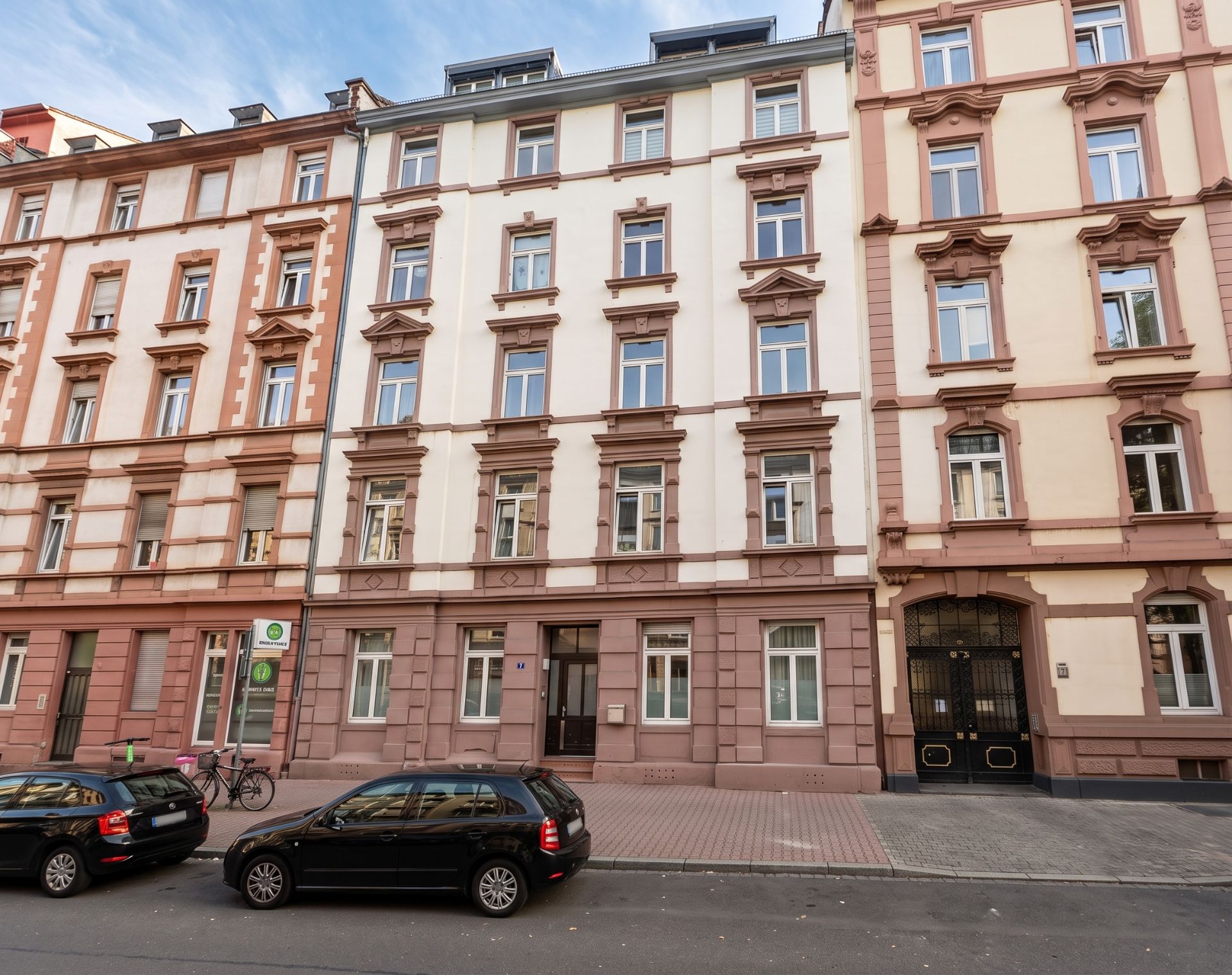 Mehrstöckiges Wohnhaus mit heller Fassade und geparkten Autos davor.