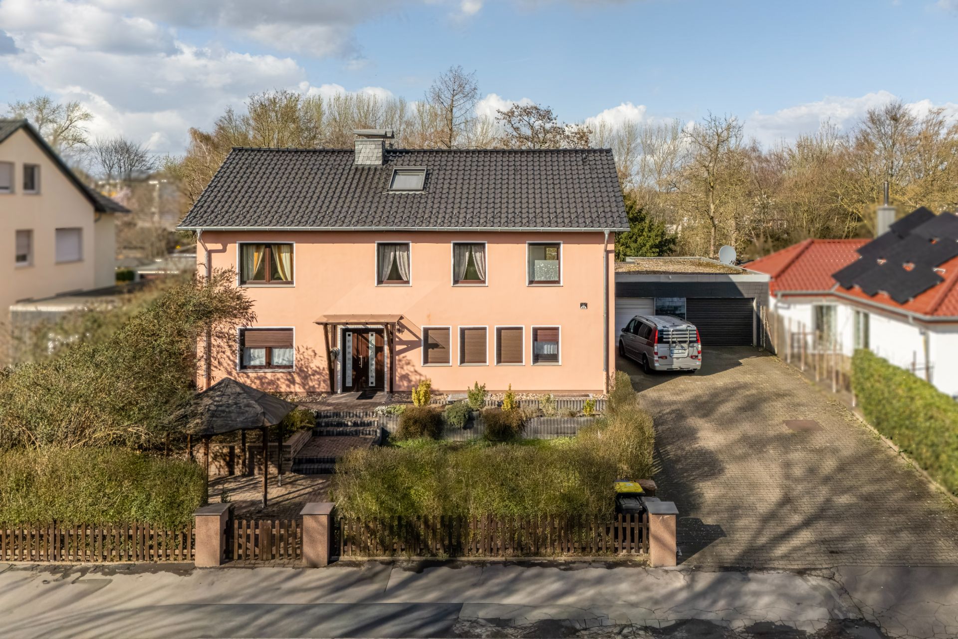 Zweistöckiges Haus mit Garten, Auffahrt und parkendem Auto vor einer Garage.