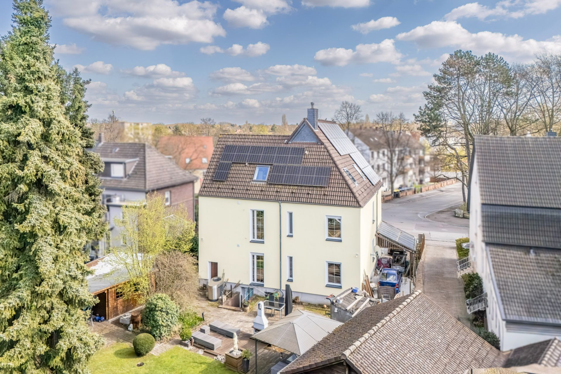 Zweistöckiges Wohnhaus mit Solarpanels auf dem Dach, Garten und Terrasse im Vordergrund.