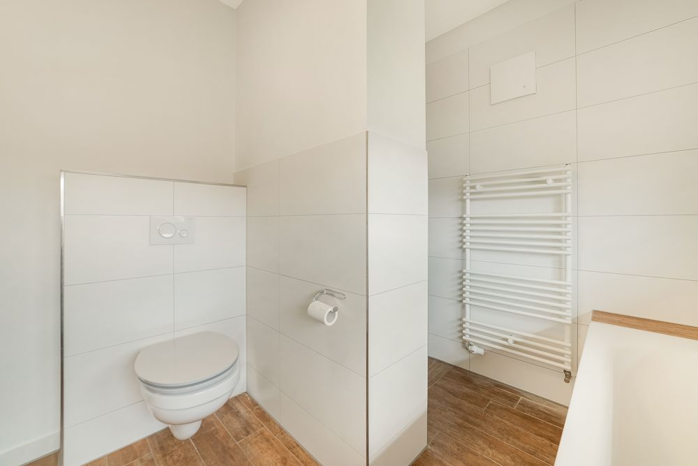 Modernes Badezimmer mit Wand-WC, weißem Heizkörper und Badewanne auf Holzfliesenboden.