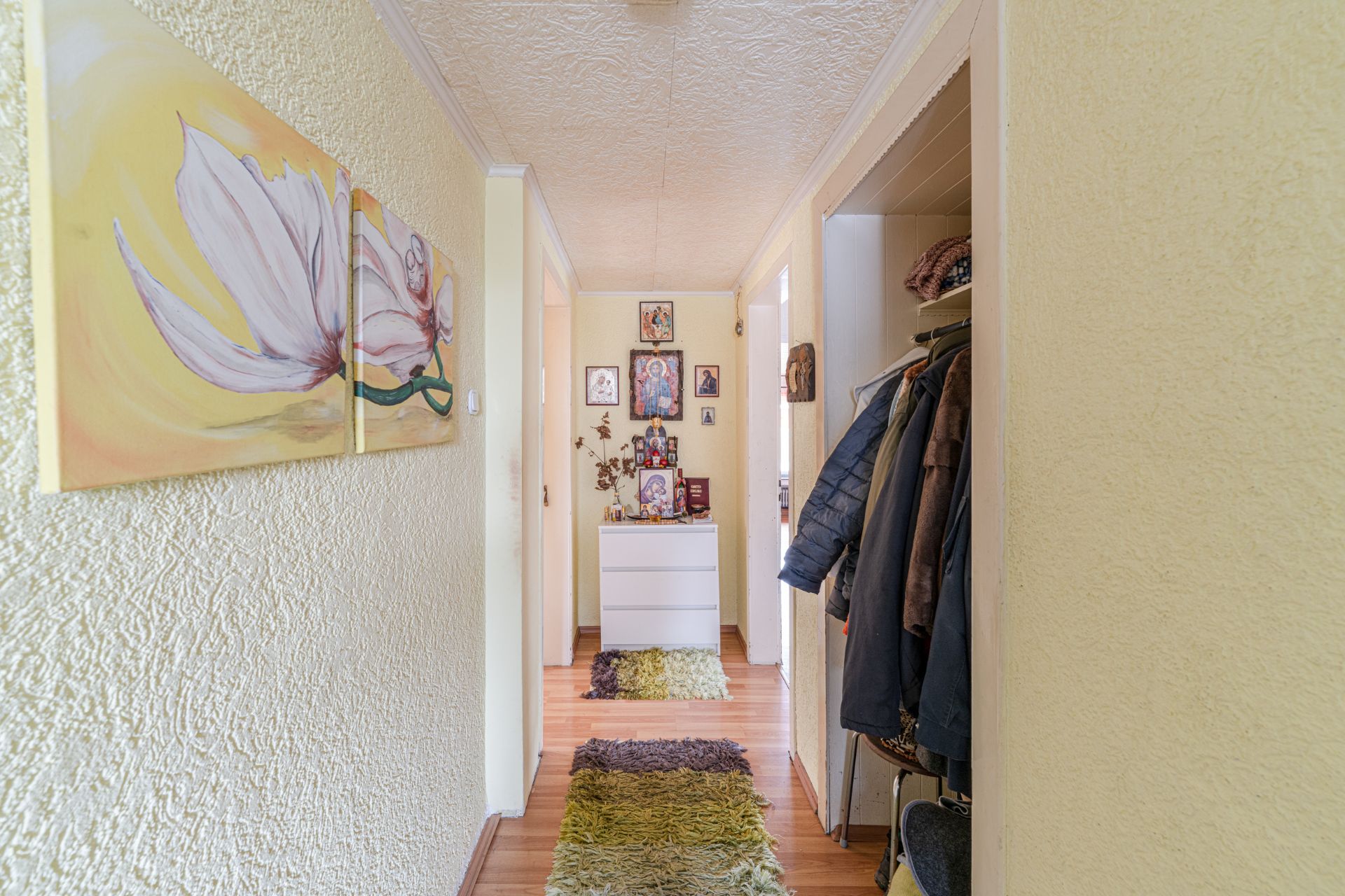 Heller Flur mit Teppichen, Garderobe, Blumenbild und Kommode mit Dekorationen.