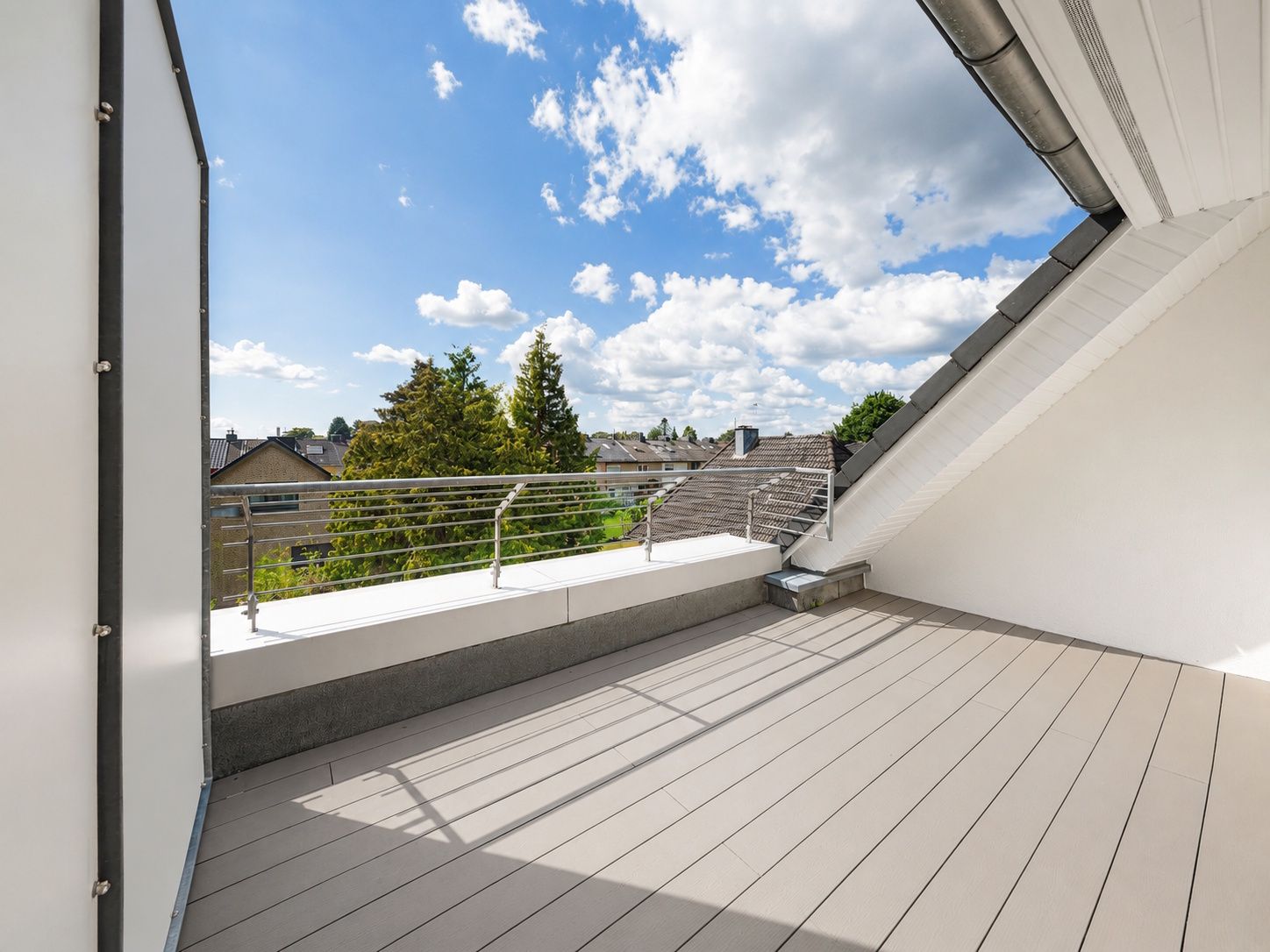 Große Dachterrasse mit Geländer und Blick auf Bäume und Nachbarhäuser bei sonnigem Wetter.