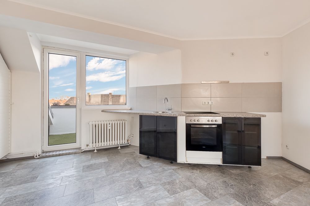 Helle Küche mit Herd, Spüle, Glasfront-Schränken und großem Fenster mit Tür zum Balkon.