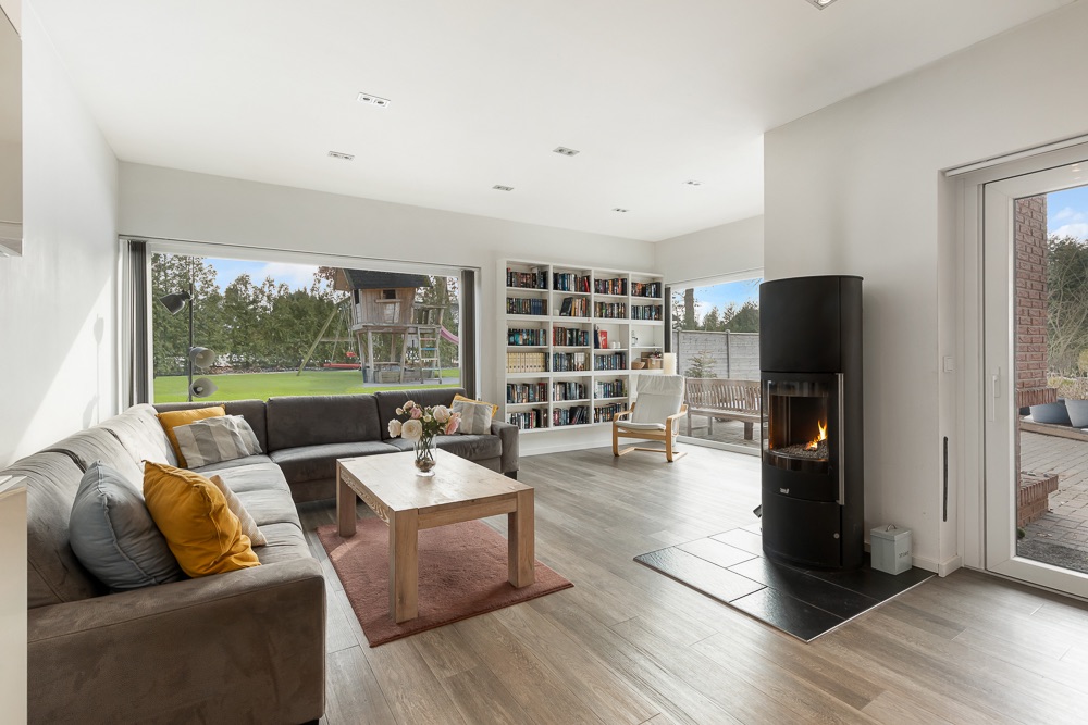 Modernes Wohnzimmer mit Sofa, Couchtisch, Kamin, Bücherregal und großen Fenstern zum Garten.