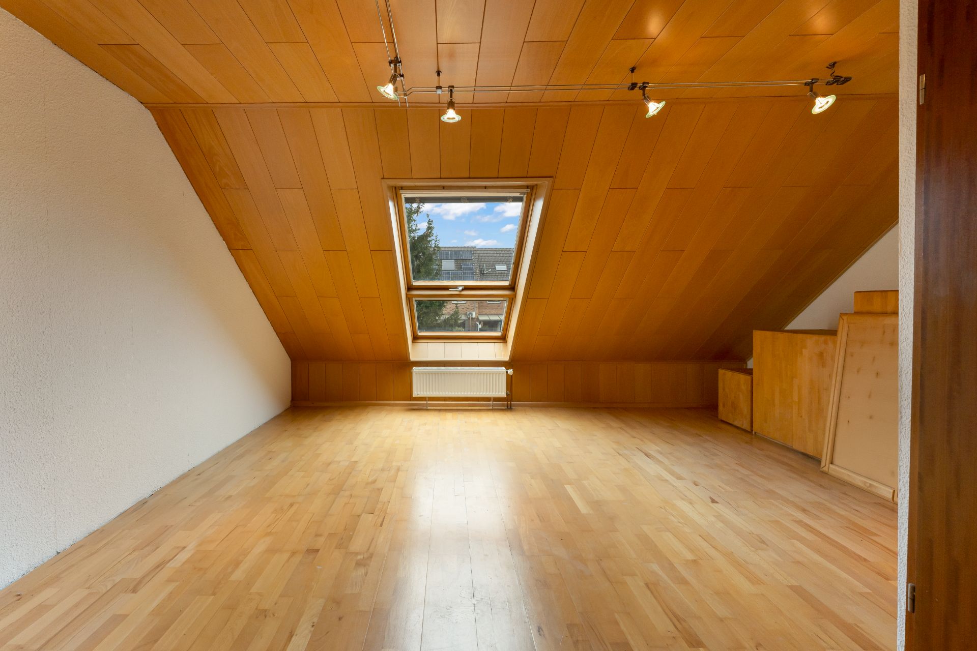 Dachzimmer mit Holzdecke, Holzfußboden und großem Fenster in der Schräge.