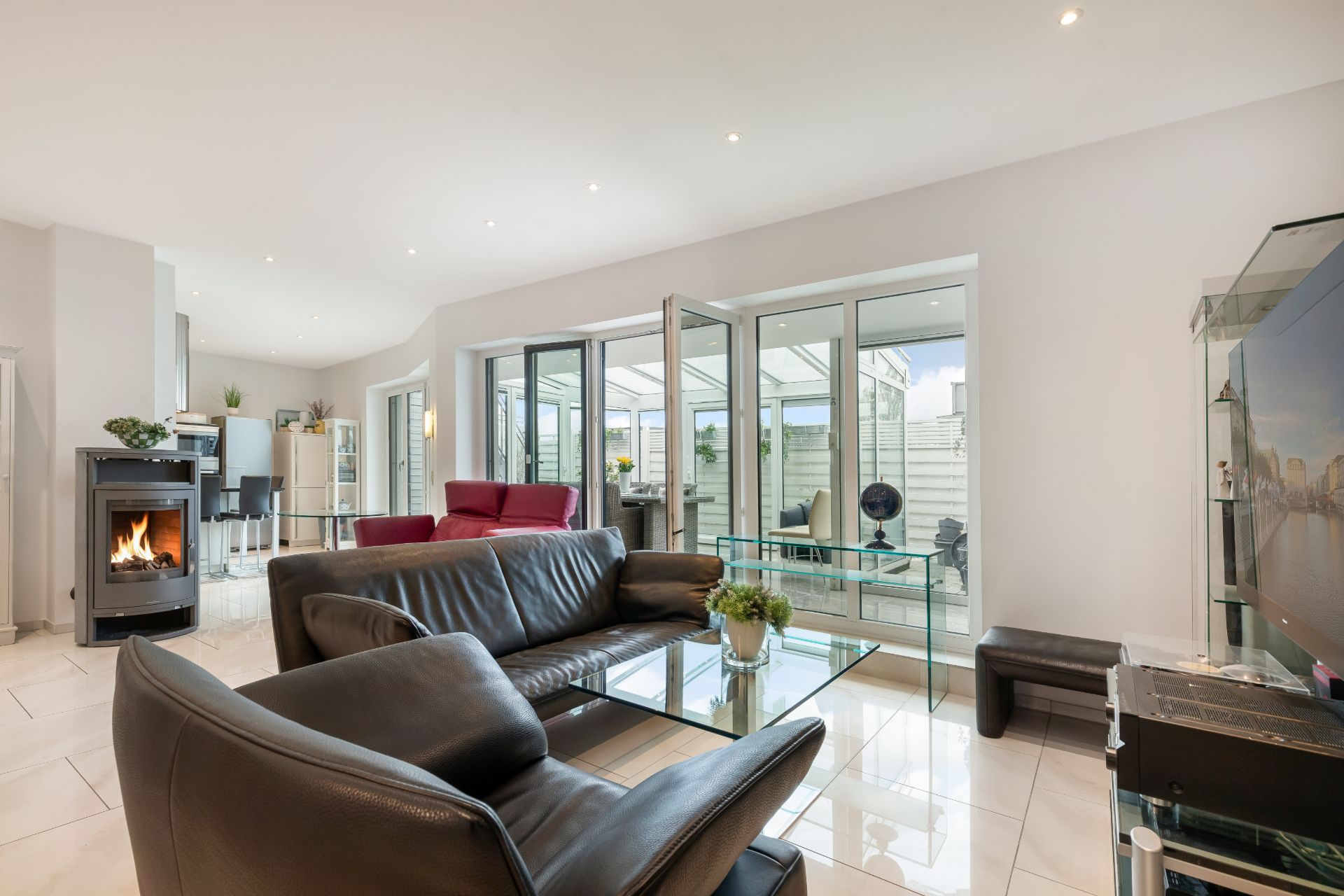 Modernes Wohnzimmer mit Ledersofa, Kamin, Glastisch und Zugang zur Terrasse.