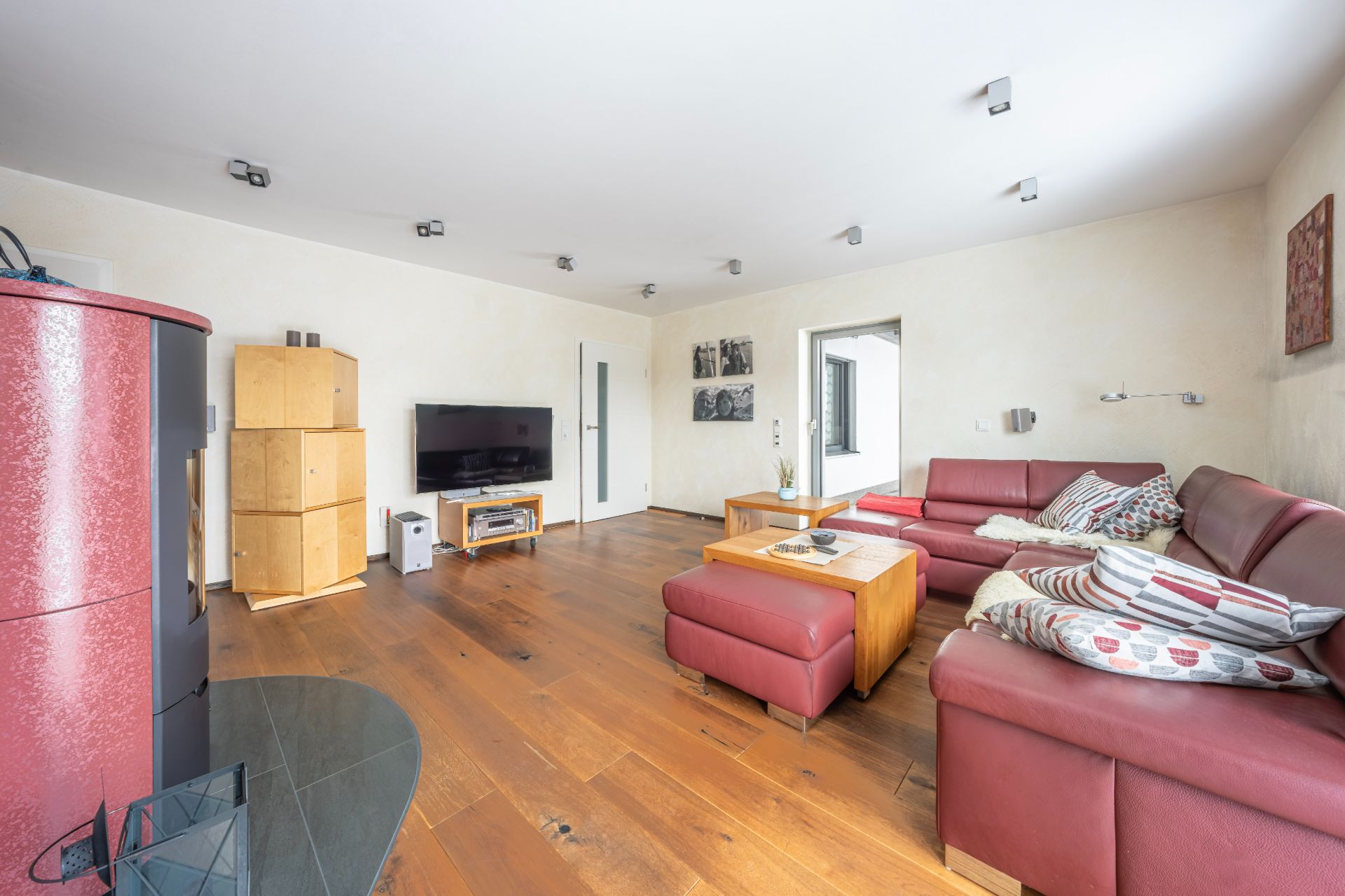 Wohnzimmer mit roten Ledersofas, Holzboden, Fernseher und Holzofen.