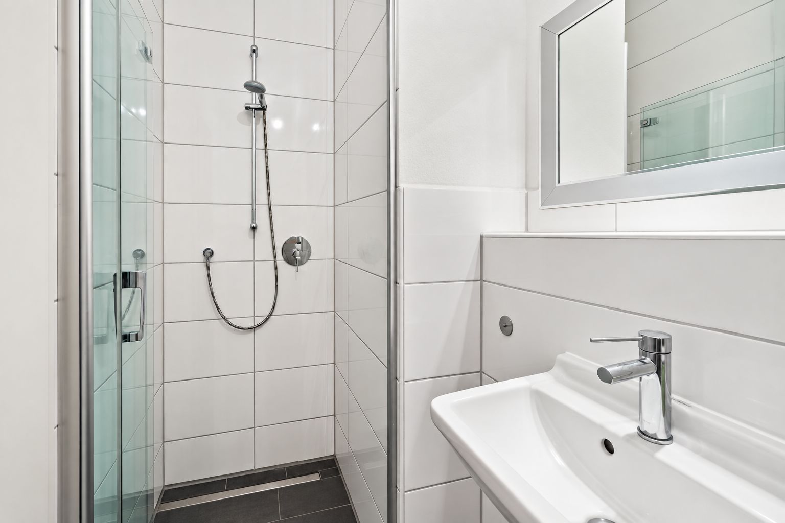 Modernes Bad mit Glasdusche, weißen Fliesen, Waschbecken und Spiegel.